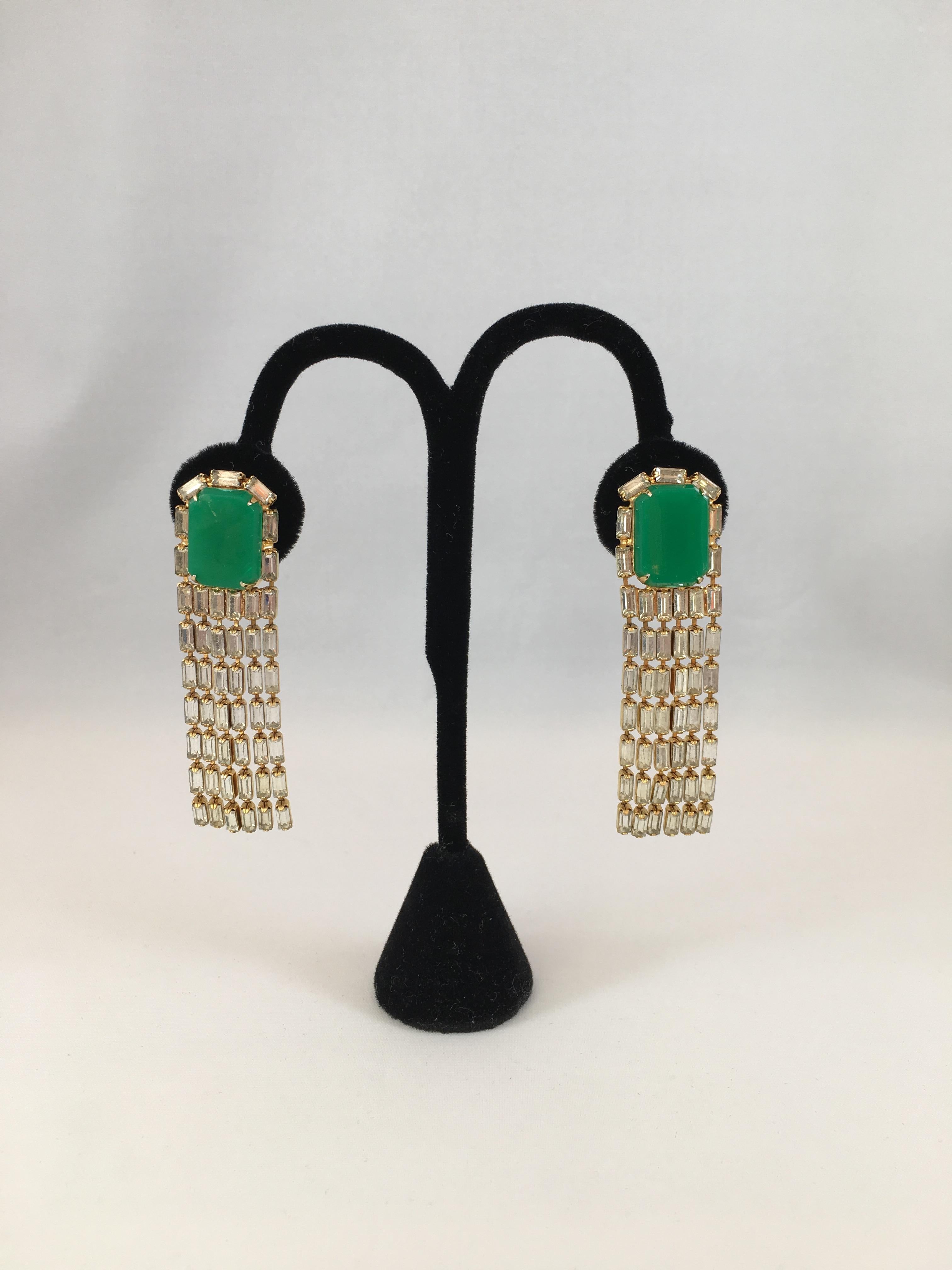 This is a super fun pair of 1970s Kenneth Jay Lane geometric clip-on chandelier earrings. Each earring is made up of a green resin rectangle shaped stone from which six strands of clear rectangle shaped glass crystals hang down. The earrings measure