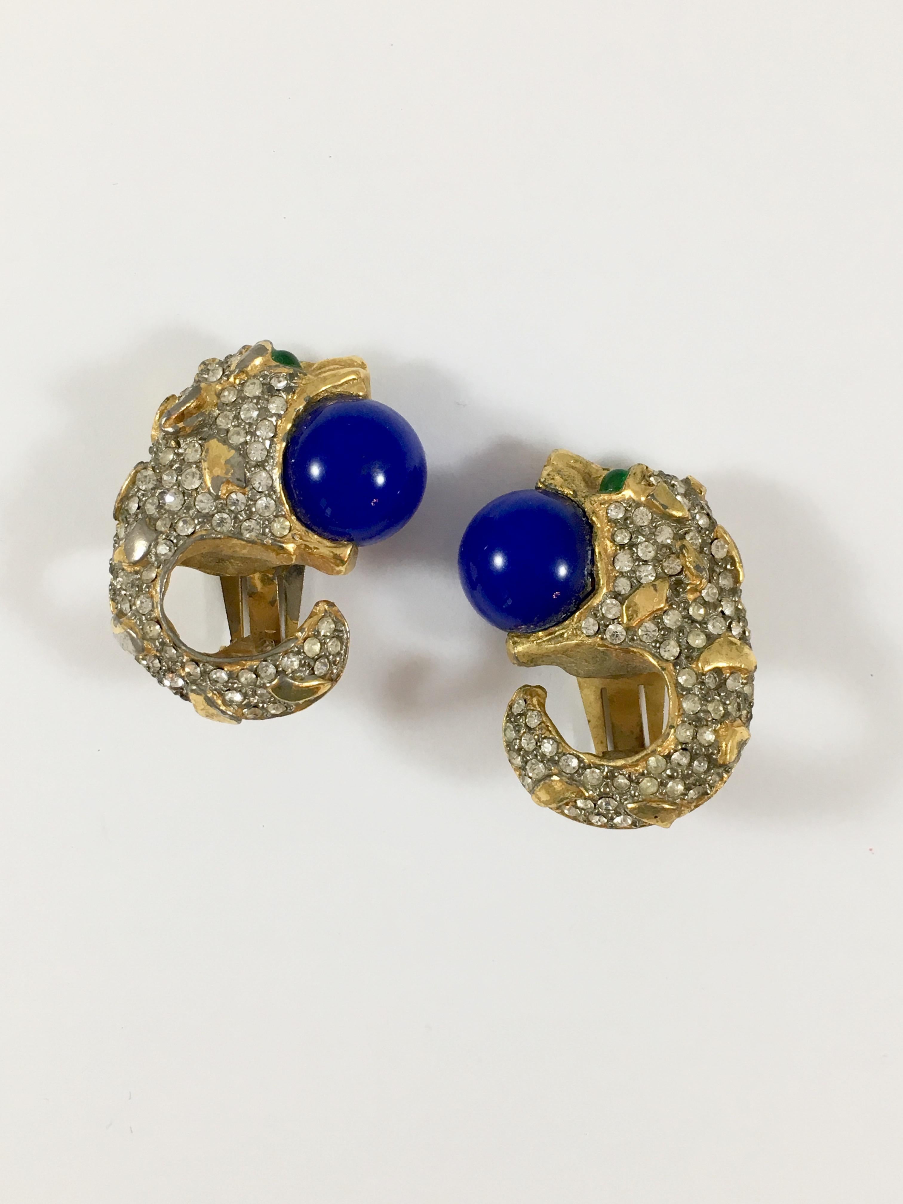 This is a unique pair of of 1960s Kenneth Jay Lane clip-on earrings. Each earring is in the shape of a paved animal head with green glass eyes and a round blue ball in its mouth - so fun, unique and well made. Each earring measures 1 1/2 inches long