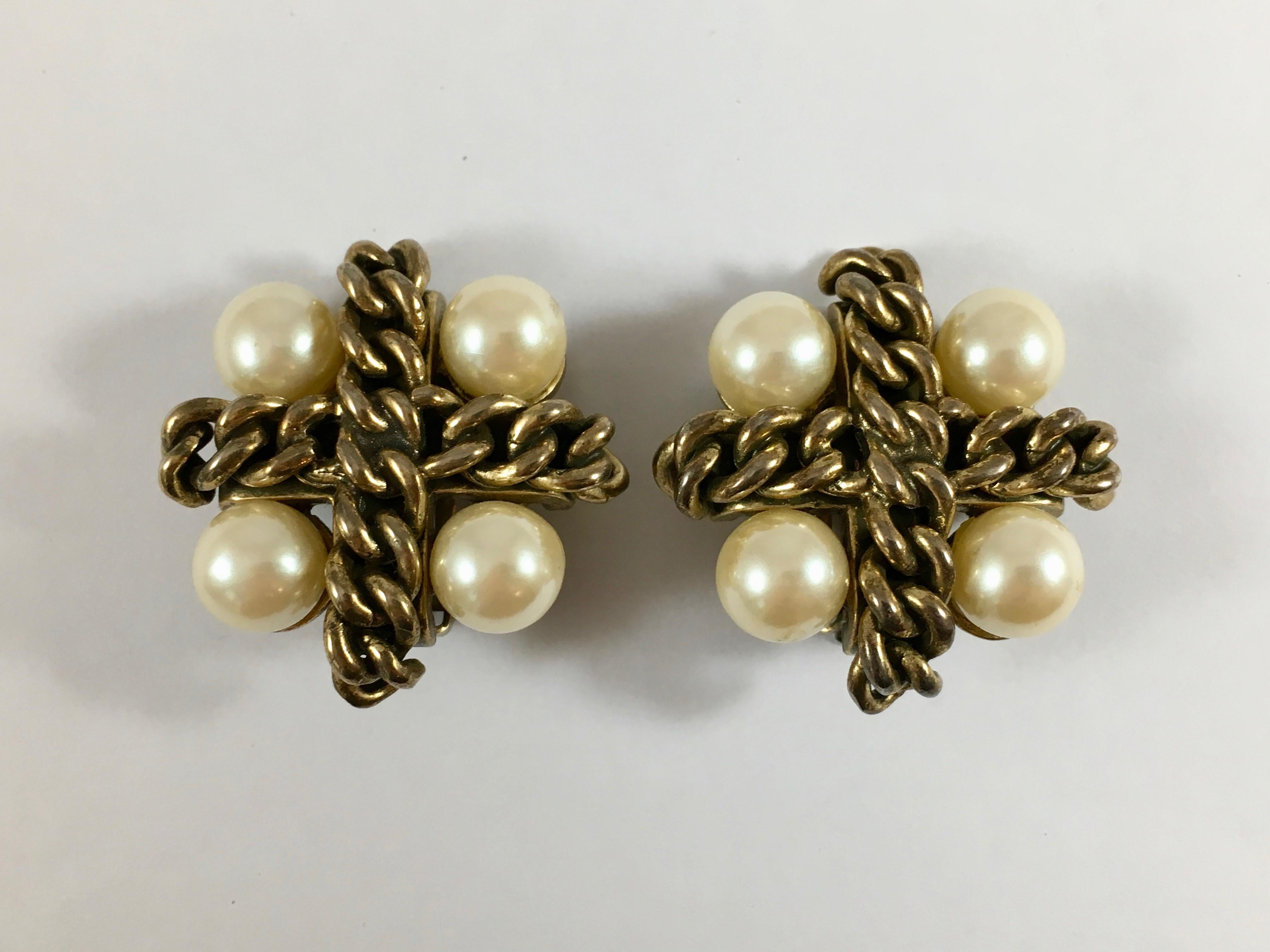 This is a pair of 1970s Kenneth Jay Lane cross clip-on earrings. They are each made out of antiqued metal chain flanked by four pearls. They measure 1 1/2 inches long x 1 1/2 inches wide. One of the earrings is marked 'Kenneth Lane' on the back.