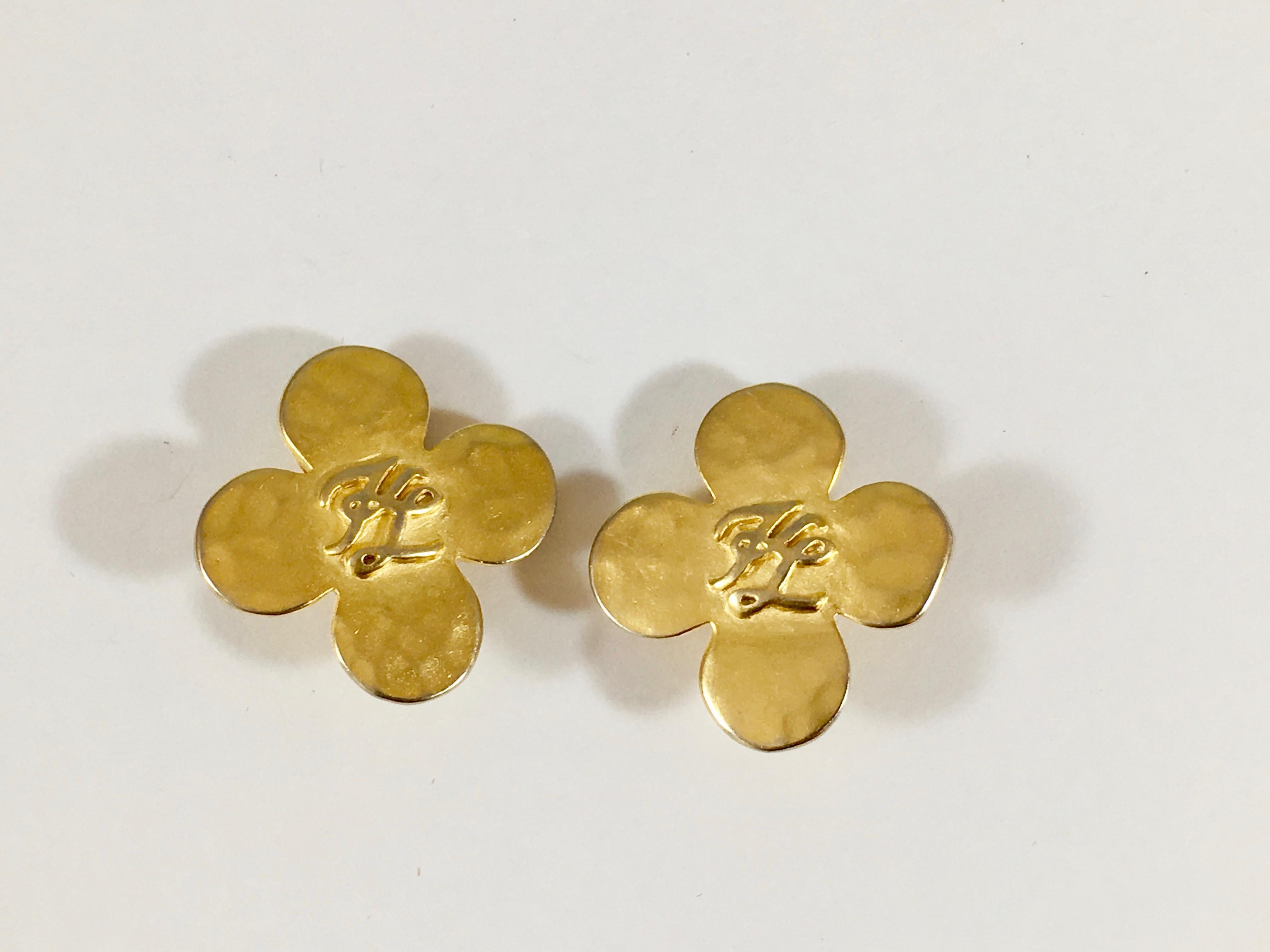 This is a goldtone pair of 1990s Karl Lagerfeld four leaf clover earrings marked in the center with a 'KL' for Karl Lagerfeld. They measure 1 1/16 inches x 1 1/16 inches. The back of each earring is marked with Karl Lagerfeld's signature fan and