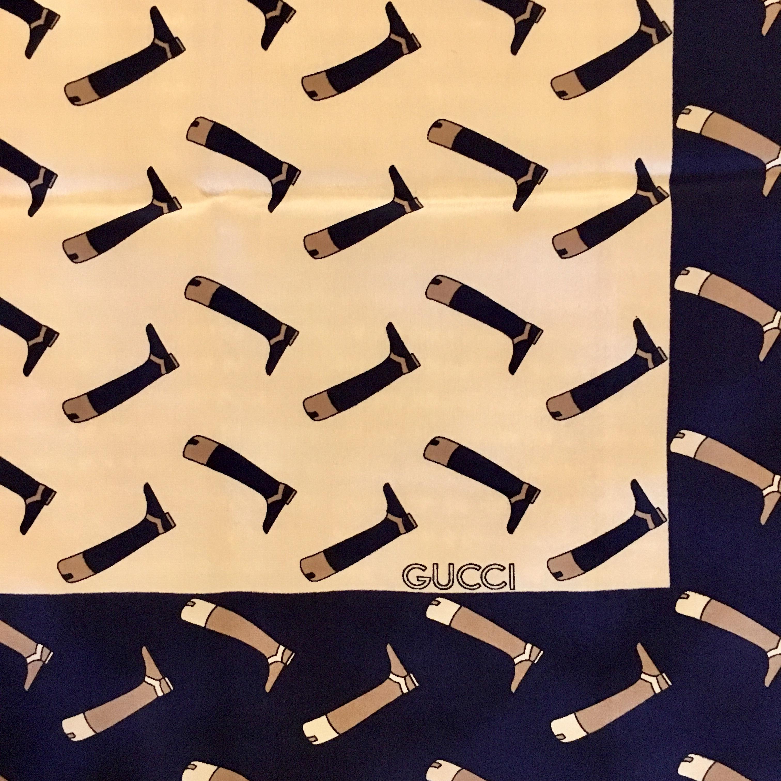 This fabulous 1976 silk Gucci scarf features a riding boot pattern. The main body of the scarf is cream with navy boots printed on it. It has a contrasting navy border with tan riding boots. It measures 35 inches x 32 1/8 inches. It is in excellent