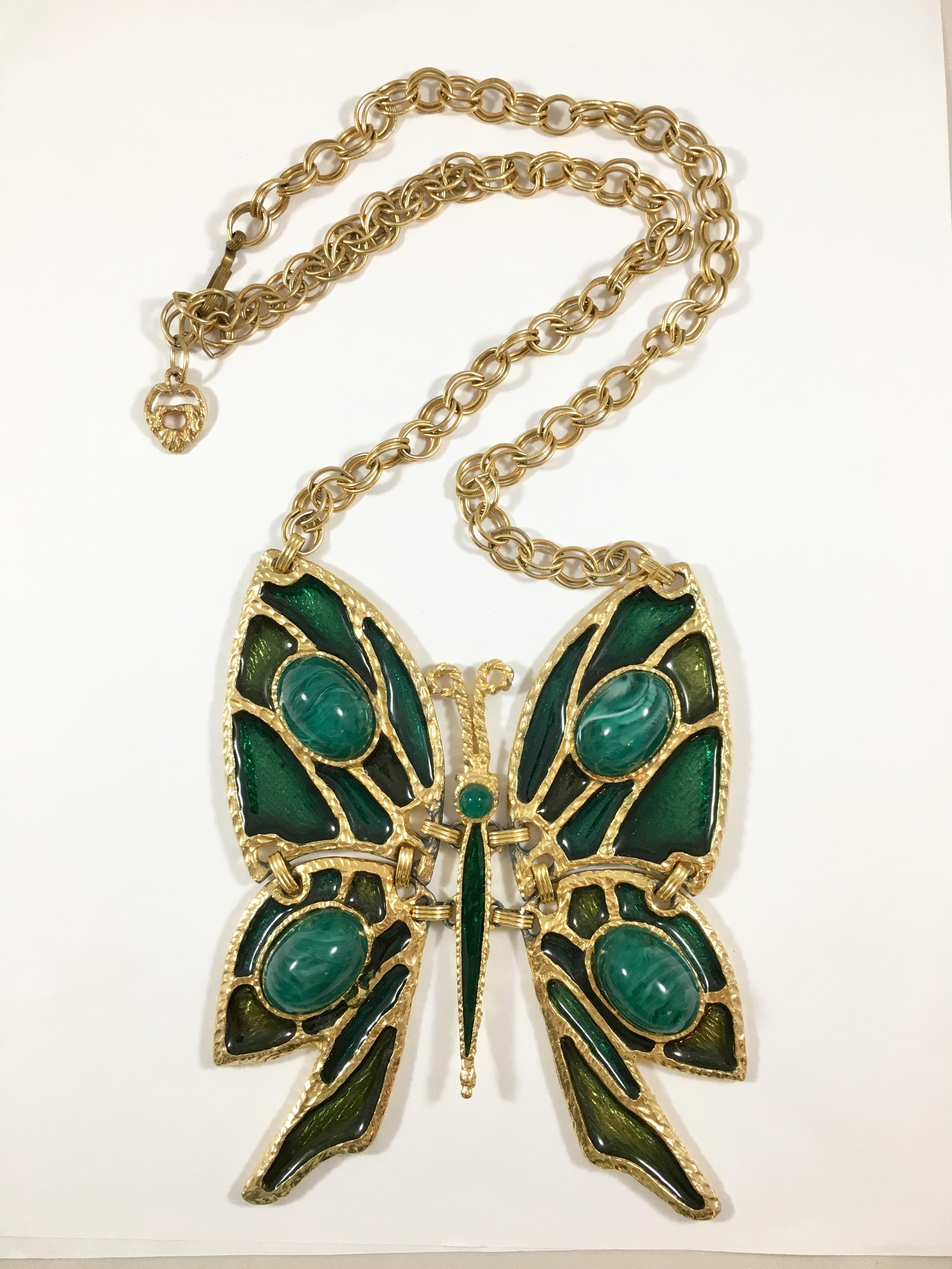 This is a massive articulated butterfly pendant necklace from the 1970s. The butterfly pendant is made out of a green enameled gold-toned metal with four green resin stones used on the wings and one resin stone used for the head. The piece makes an