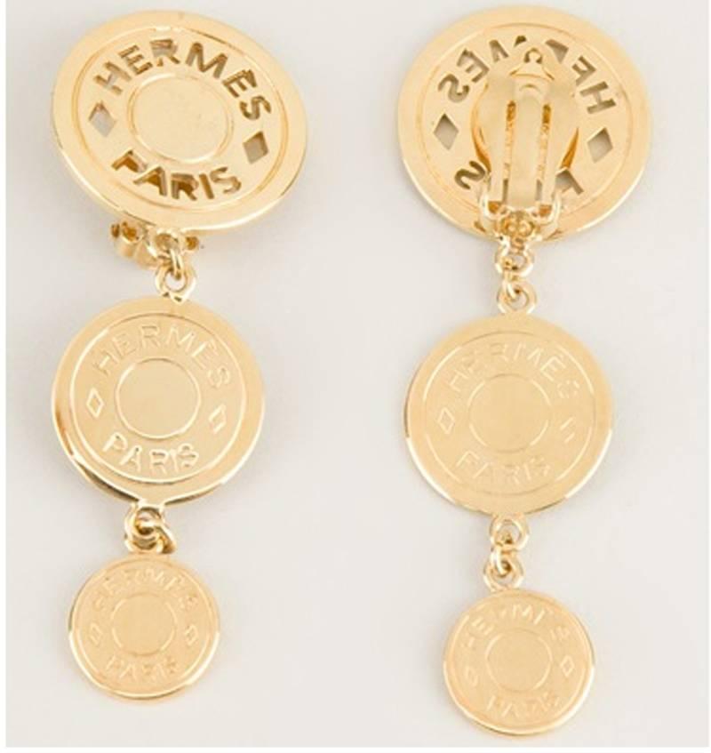 Exceptional Gold plated pendant earrings from Hermes featuring three separate designer embossed coins and a rear clip on fastening. Marked at the back: Hermès Paris Bijouterie Fantaisie. Excellent vintage condition. Size: 8 x 2.5 cm - 3 1/6 x 1 in