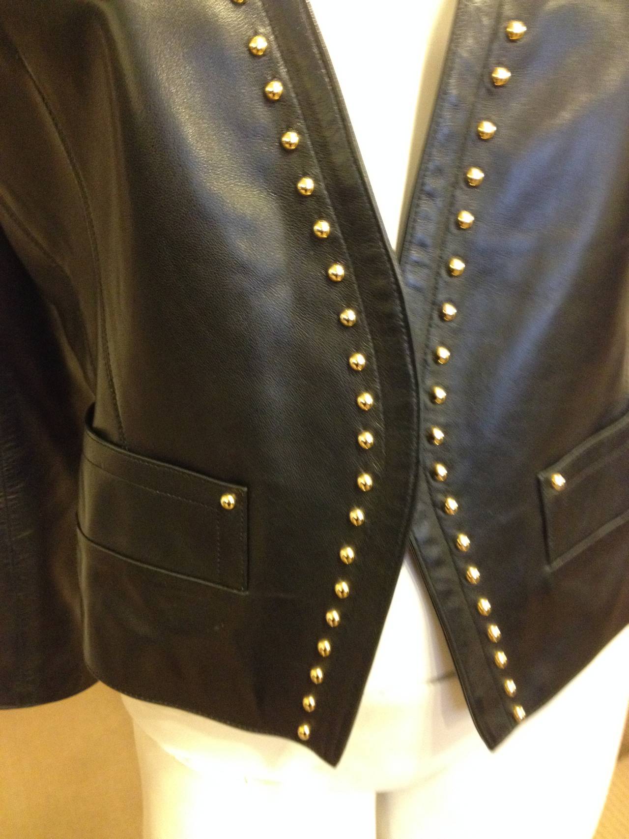Shine bright! This fabulous leather Yves Saint Laurent jacket is tailored perfectly, with structured padded shoulders and a deep v-neck. The front is punctuated with a series of little gold round studs, adding just the right cool touch. This piece