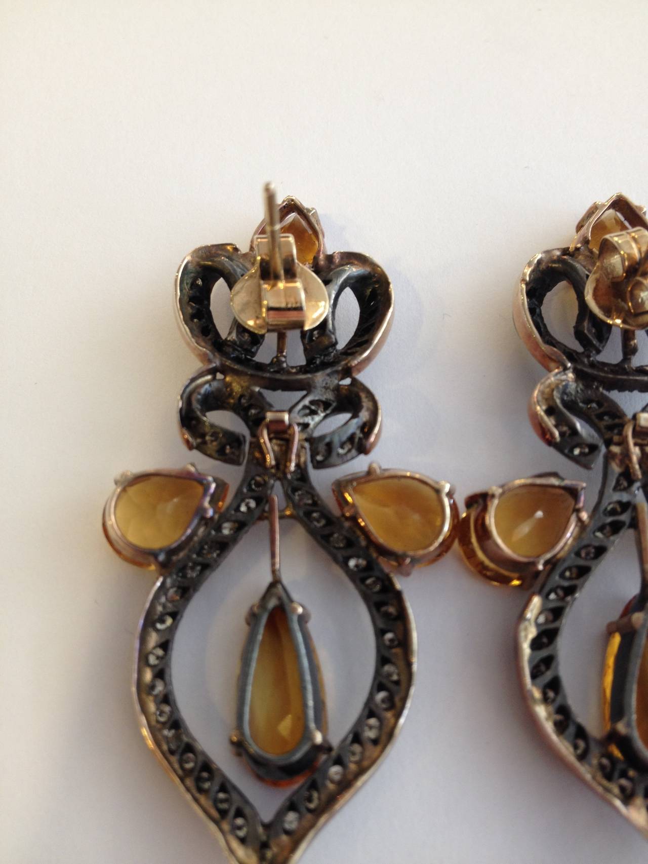 These earrings feature beautiful yellow topaz stones surrounded by diamonds, all set within curling metal ribbons.