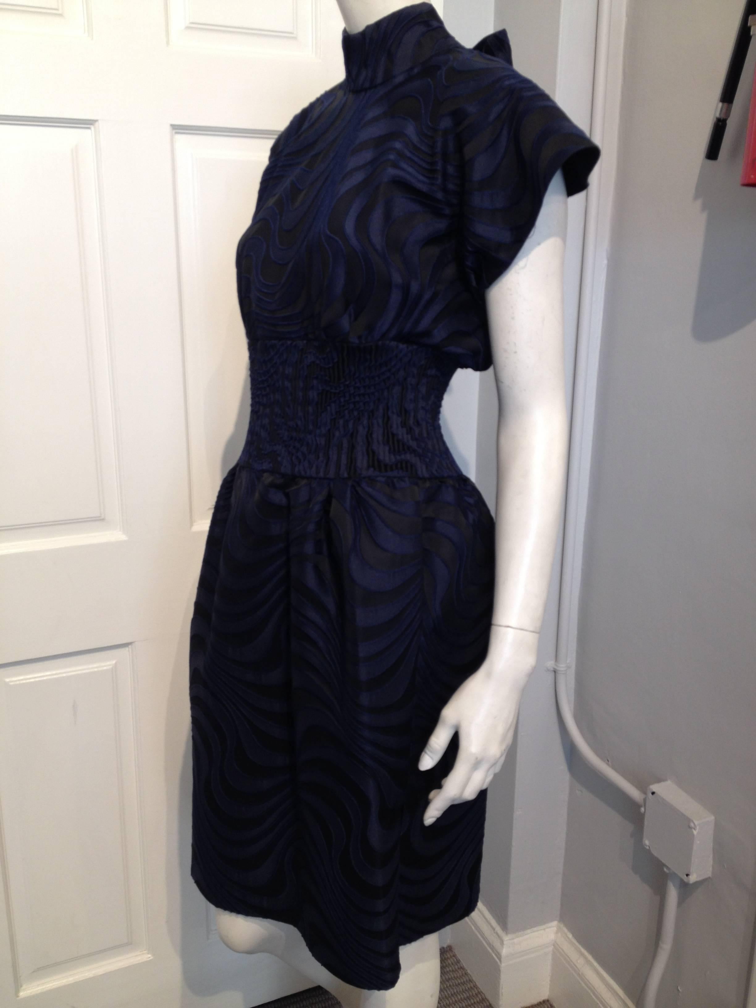 A sculptural and unique cocktail dress by Vionnet. Black and navy swirled brocade fabric. Wide cape-like flared shoulders, a ruched waistband, flared skirt, with a hidden zipper running down the back.