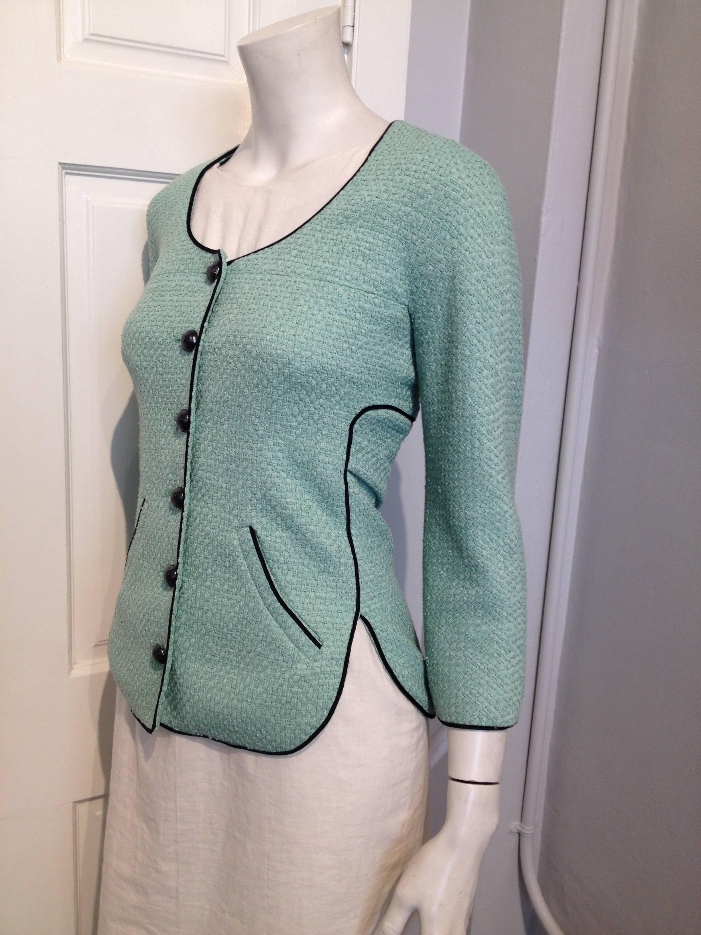 Gorgeous mint green tweed with black piping and iron grey rock shaped Chanel buttons, cut slim with a round neck, three-quarter sleeves, and a shirt-tail hemline.