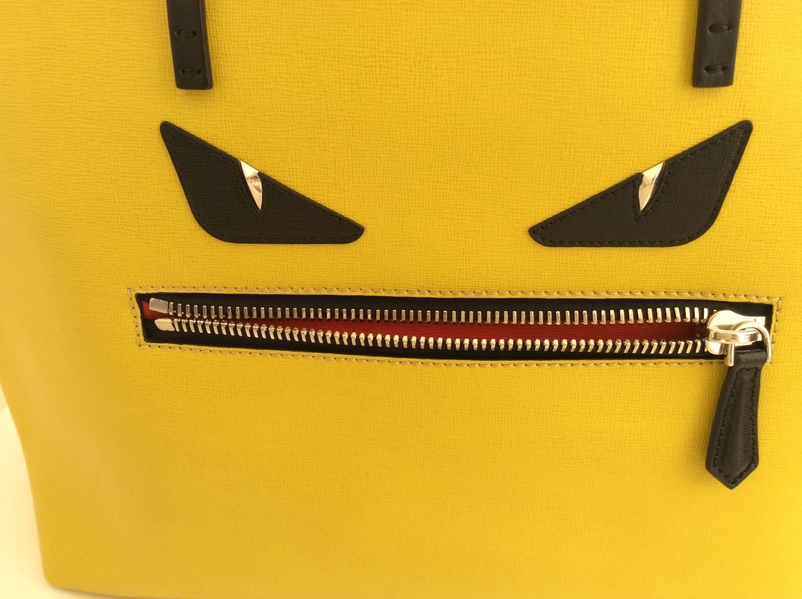 Fendi medium Monster Roll tote in yellow leather with two black leather shoulder straps (9.5” drop). Two black leather eyes and a black surrounded zipper pocket - lined in red - create the ‘monster’ face. The interior is lined in black fabric and