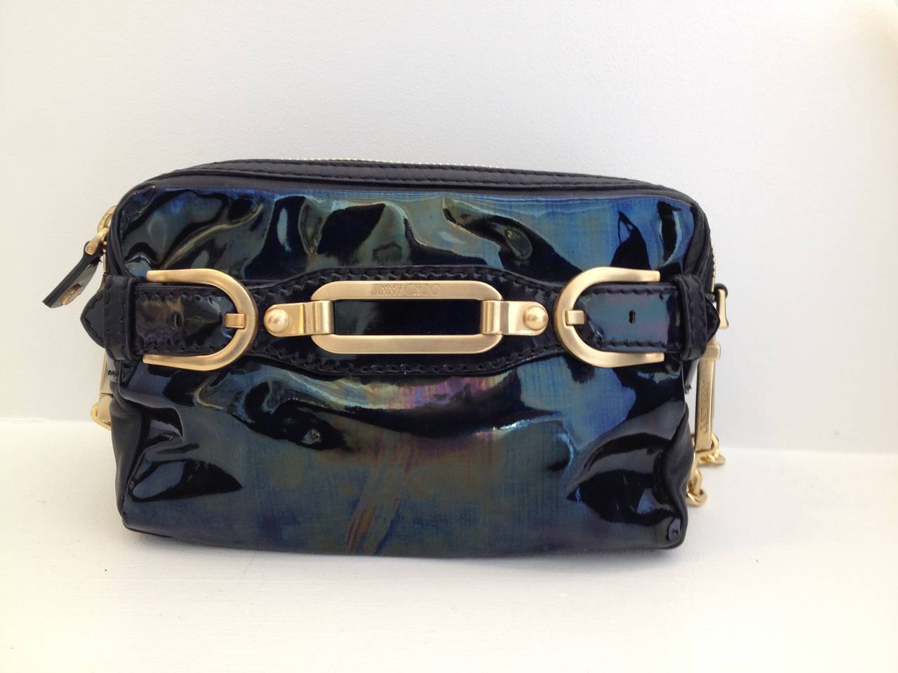 What a fun little purse! This Jimmy Choo bag combines an iridescent patent front with buttery soft black leather, outfitted with oversized gold buckles and chain hardware. The long 14 inch drop strap is detachable so you can carry it either over