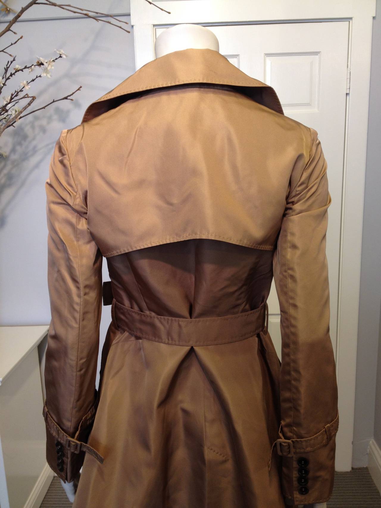 This is the coat for a true femme fatale. More curvy and stylized than a traditional trench coat, it features an asymmetrical line of buttons down the front that creates a dramatic angular opening toward the hemline, and accentuates the waist. The