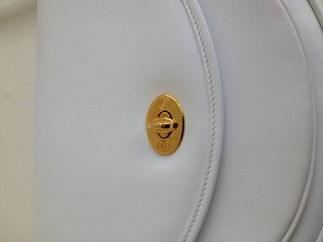 Smooth white leather and glossy gold hardware make this classic Gucci bag extra special. Small and compact with a semi-circular style, it features a long strap that measures 19.5 inches from the top of the bag. The interior is lined in a soft brown