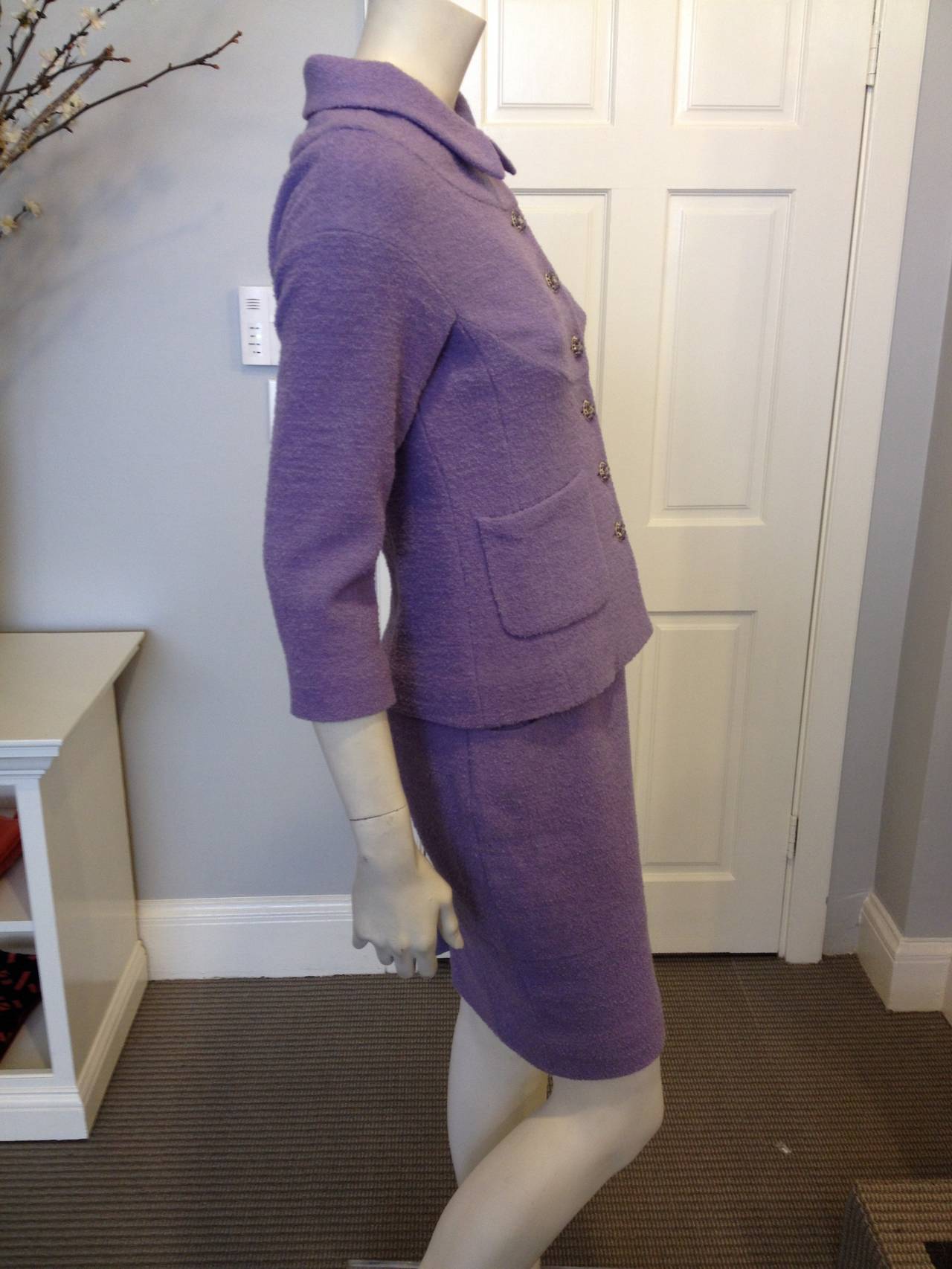 This very feminine Chanel suit is so elegant. The high collar is slightly wider than it is deep and features a boat neck style seam running around the shoulders. Each hip has a diagonally cut pocket. Running down the front of the jacket is a line of