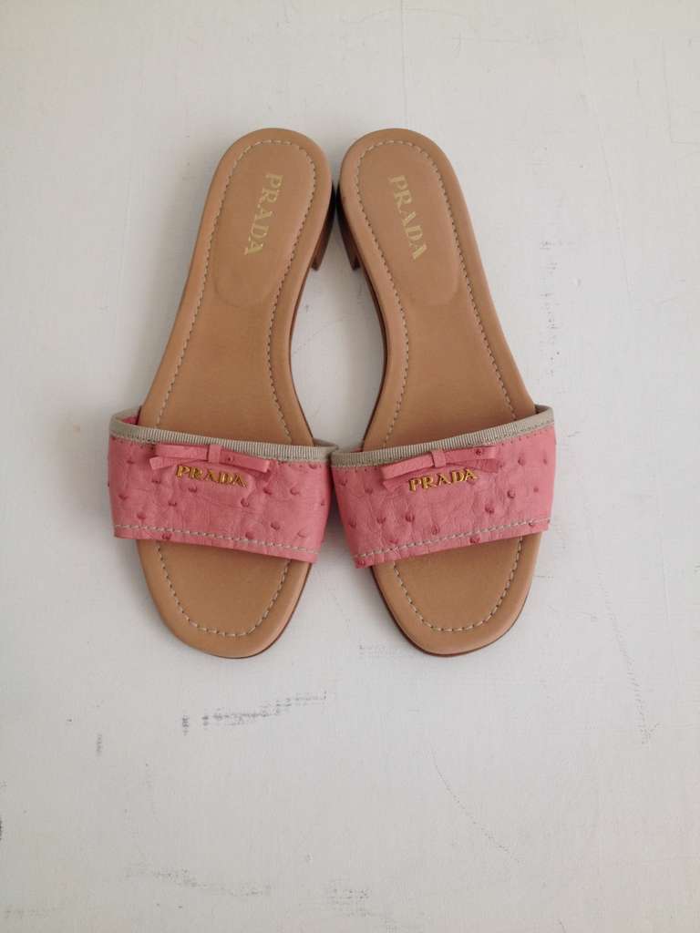 These slides are anything but ordinary! This typically easy, comfortable shoe is dressed up with a fun, feminine bright pink ostrich leather strap, grosgrain trim, little leather bow, and gold PRADA logo. Propped up on a half-inch heel, they're