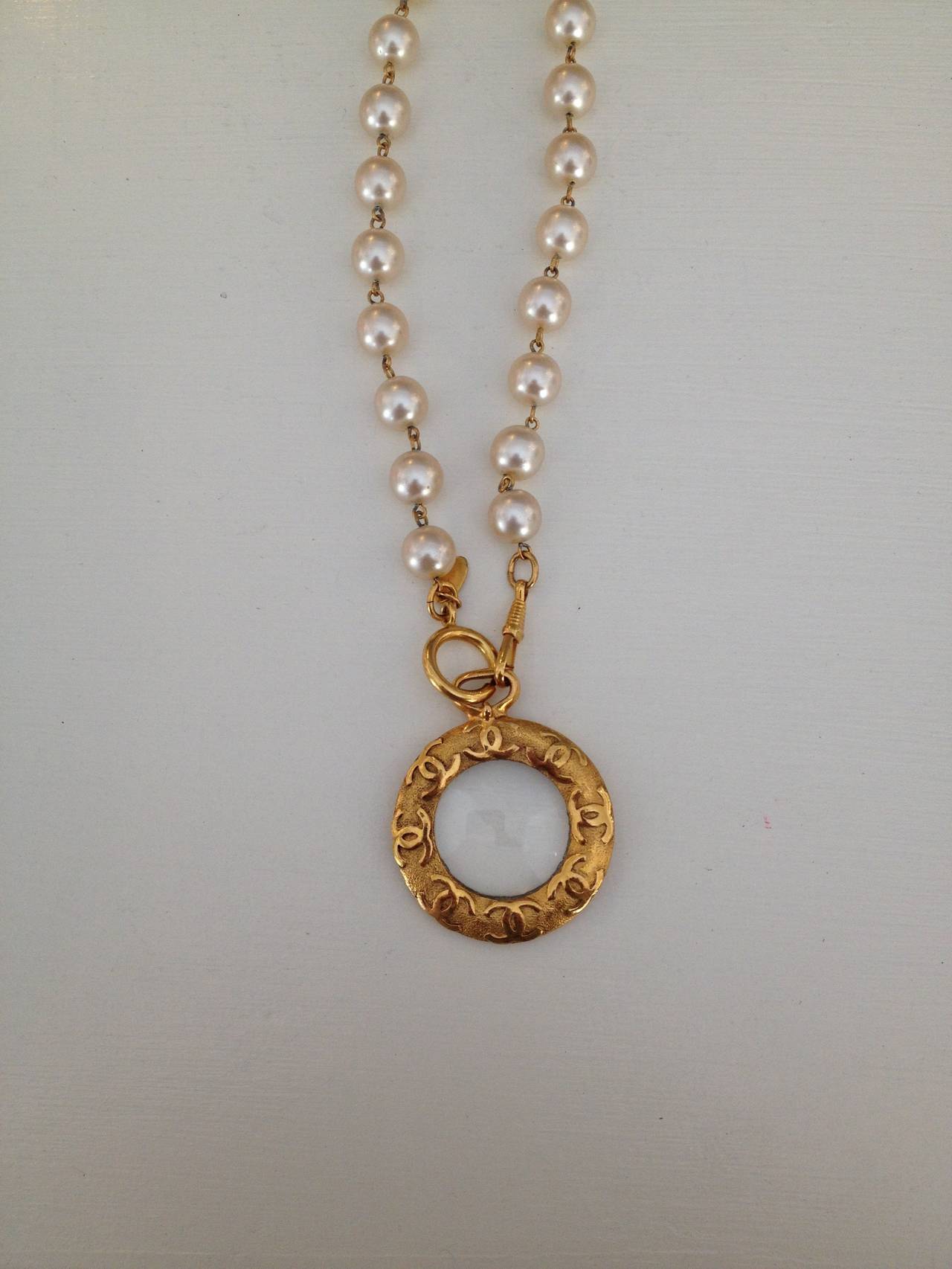 Add a classic and elegant accent to your look by accessorizing with this pearl Chanel necklace. The gold tone magnifying glass pendant with iconic monogram makes this piece distinctive. Perfect over a shirt dress, or setting the tone for a more