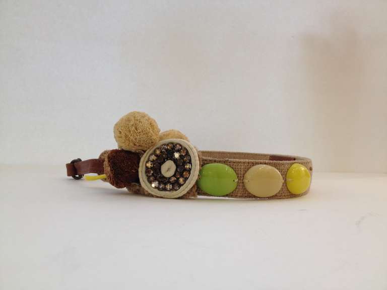 This belt adds just the right amount of candy! The playful and pretty assortment of baubles on this woven Marni belt include raffia pom-poms, a bejeweled brooch, and three oversize beads in lime, beige, and lemon yellow plastic. This belt is all you