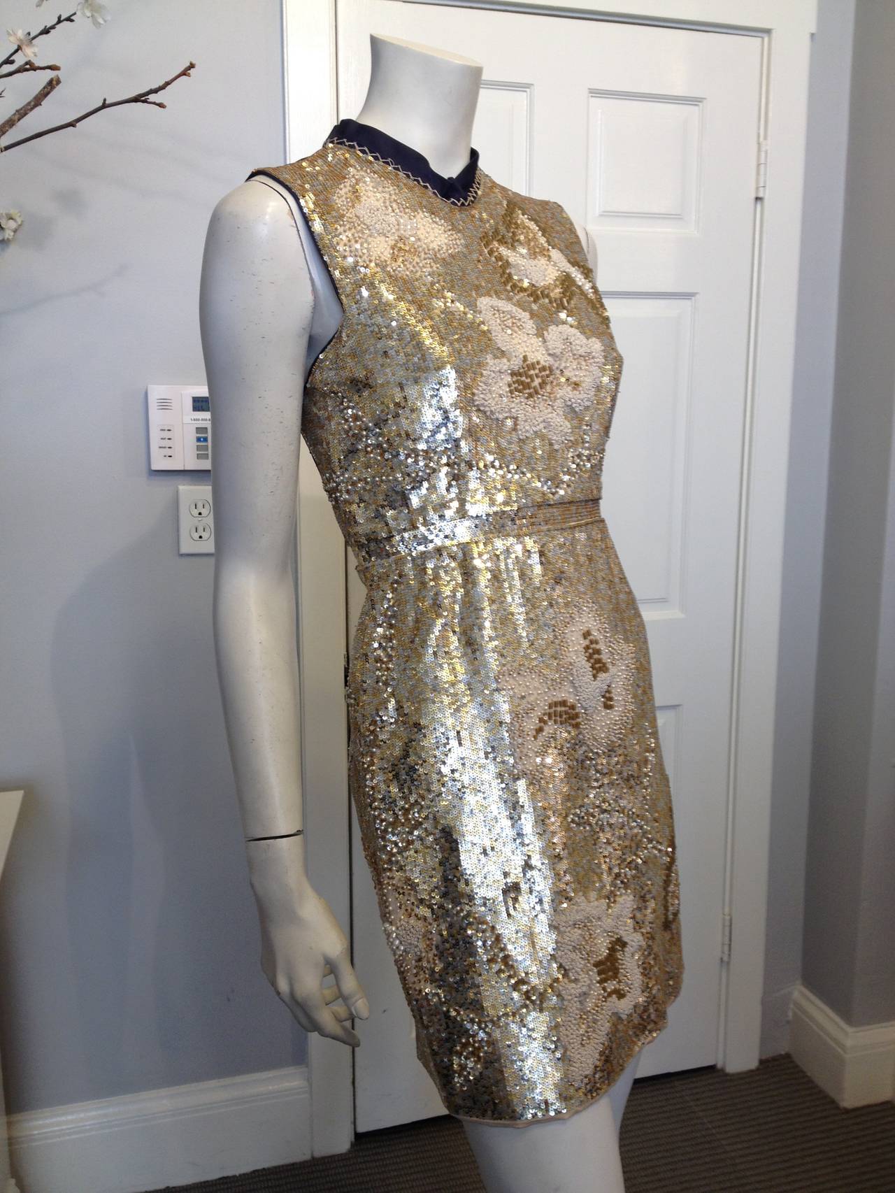 This 6267 cocktail dress is the perfect piece for making an impact. The navy satin backing is covered with a blanket of gold and silver sequins, champagne-colored embroidery, seed beads, and pearls, all of which form delicate blossoming textural