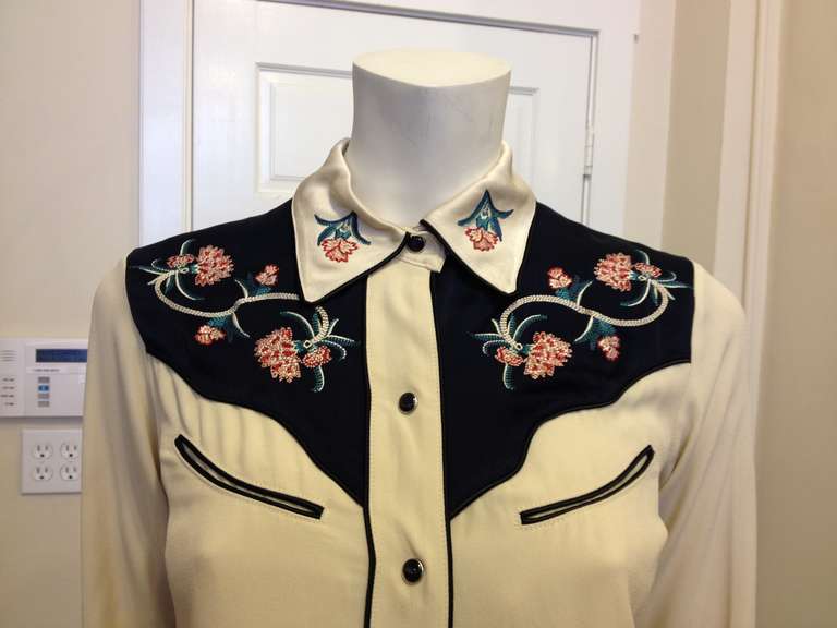 Annie, get your gun! This embroidered button up shirt is perfect for any lady, from the wild west to today. The heavy, glossy satin material is beautiful behind the carefully stitched pink carnations and elaborate green winding vines, and the piping