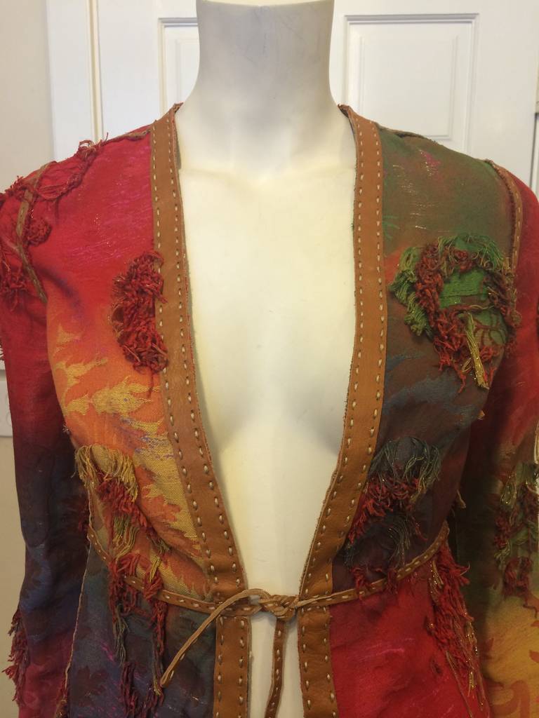 Brocade in reds, greens, and blues frays in little patches across this jacket to create an undone, avant-garde look, while leather strips accent the piece along seam lines. The single high-waisted tie in the front elongates the silhouette- this
