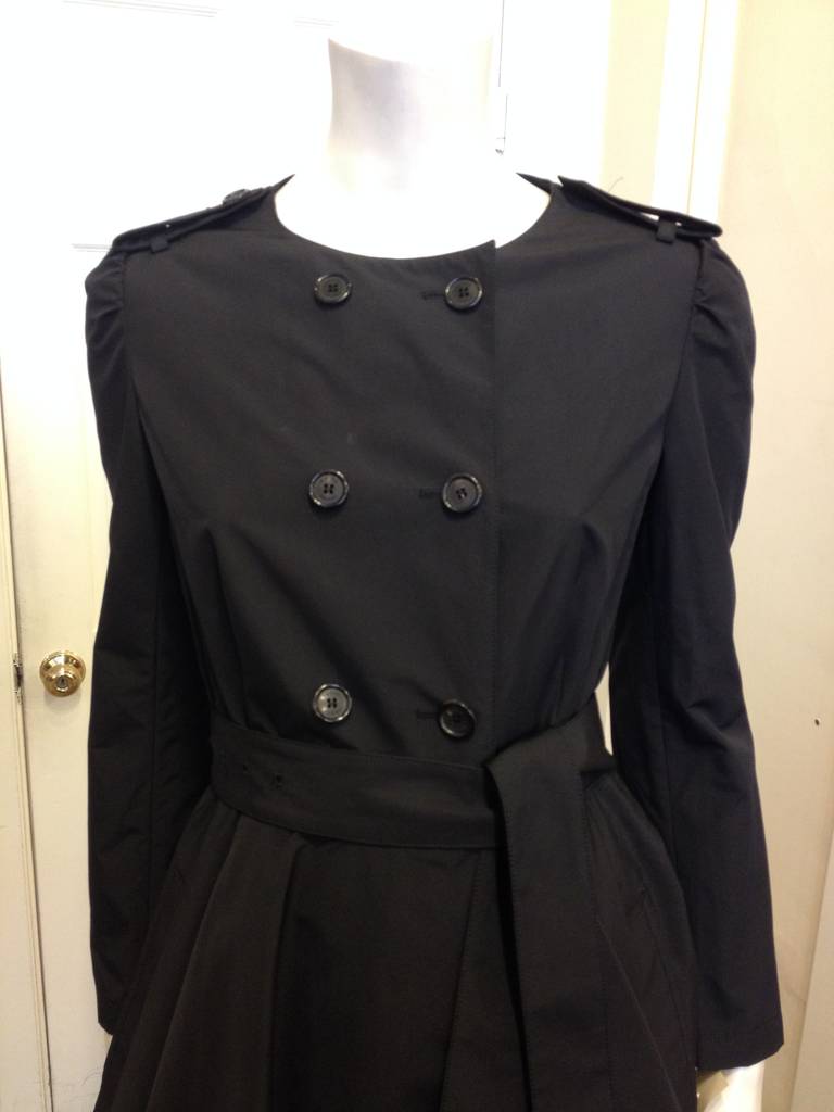 This flirty little Prada piece is timeless! The double-breasted trench coat is complete with button epaulets and a belt that cinches the waist in, while the skirt flares out adding a soft, classically feminine touch. This coat is perfect for all