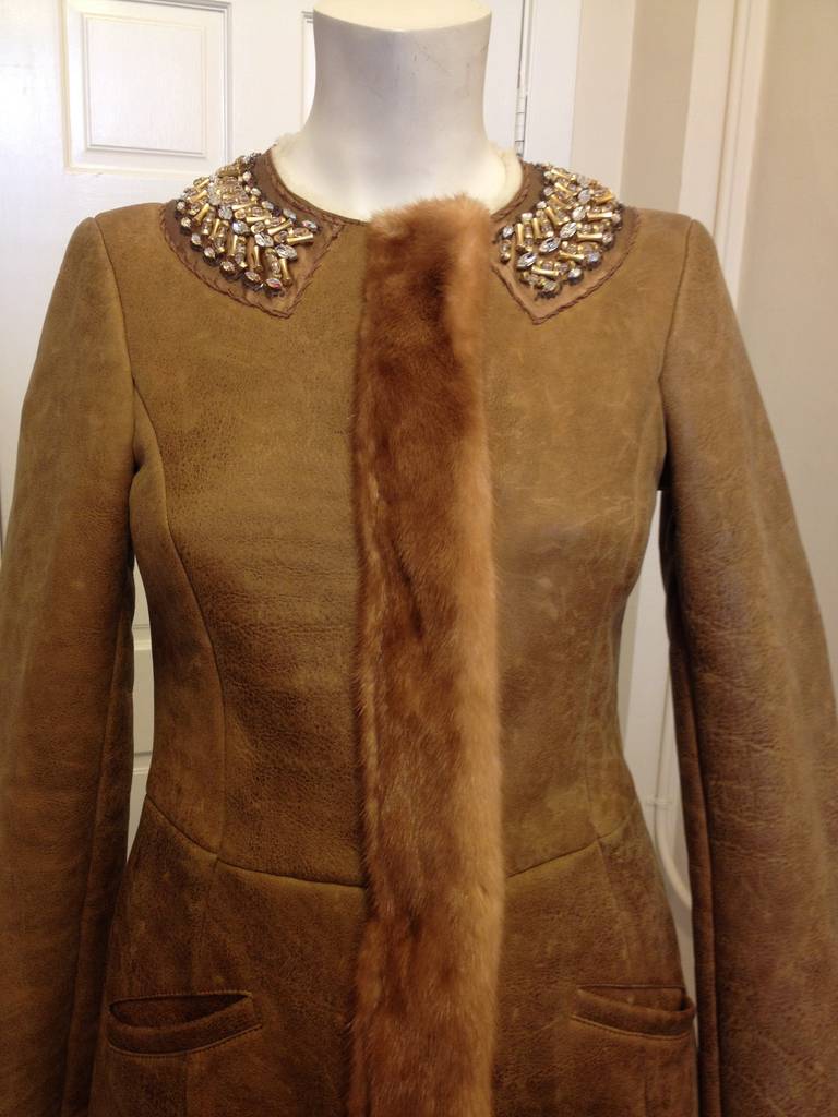 This coat is fit for a queen - equal parts rugged and splendid, it's truly a stunning piece. The body is made of sheepskin shearling, cut into a feminine fitted shape with princess seams and a tea-length hem. The round neckline is trimmed with a
