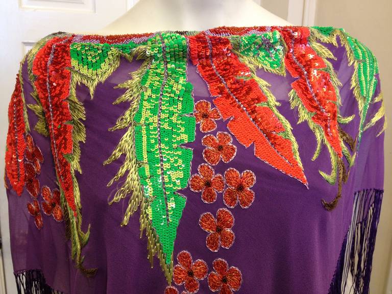 Transport yourself somewhere exotic! Hibiscus flowers and lush banana leaves in hot neon orange and bright fluorescent green sequins are arranged around the neckline, while the hem is decorated with a decadent long purple fringe. The sheer purple