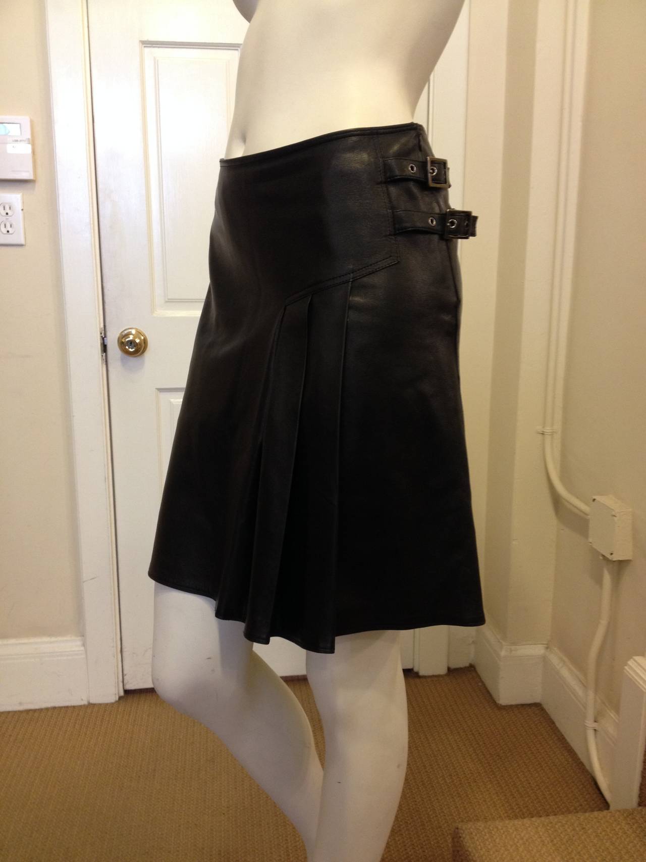 Accented with two silver buckles and three pleats on one hip, this asymmetrical black leather skirt  is certainly edgier than most of the iconic soft, sculptural, floral Dior creations. The defined but minimal silhouette borrow from classic Dior