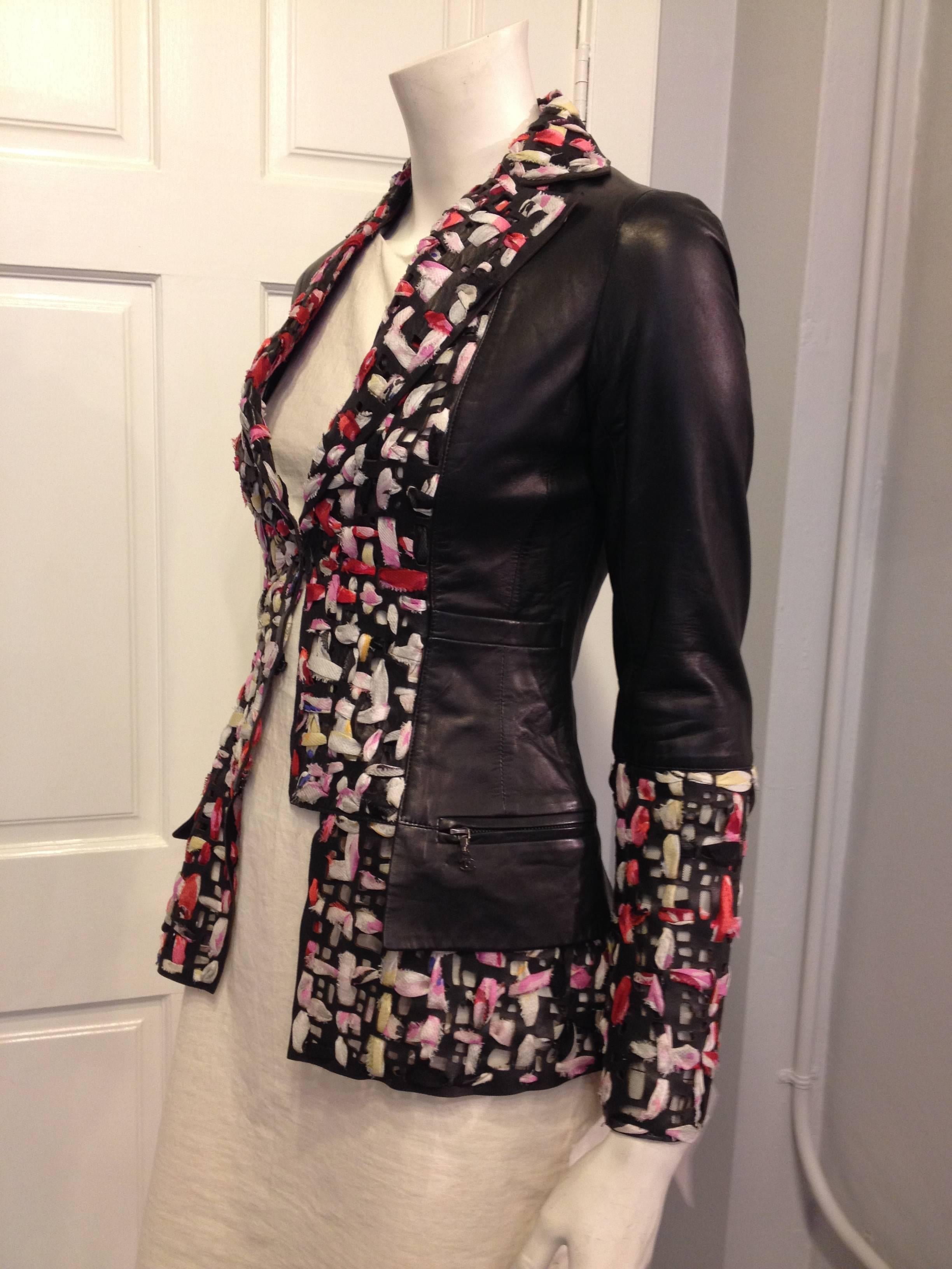 A mix of exuberant color and sharp black leather, this jacket is the perfect way to transition from one season into the next. Intricate cutouts perforating the collar, sleeve, and hem are woven with strips of lush colored silk fabric, creating a
