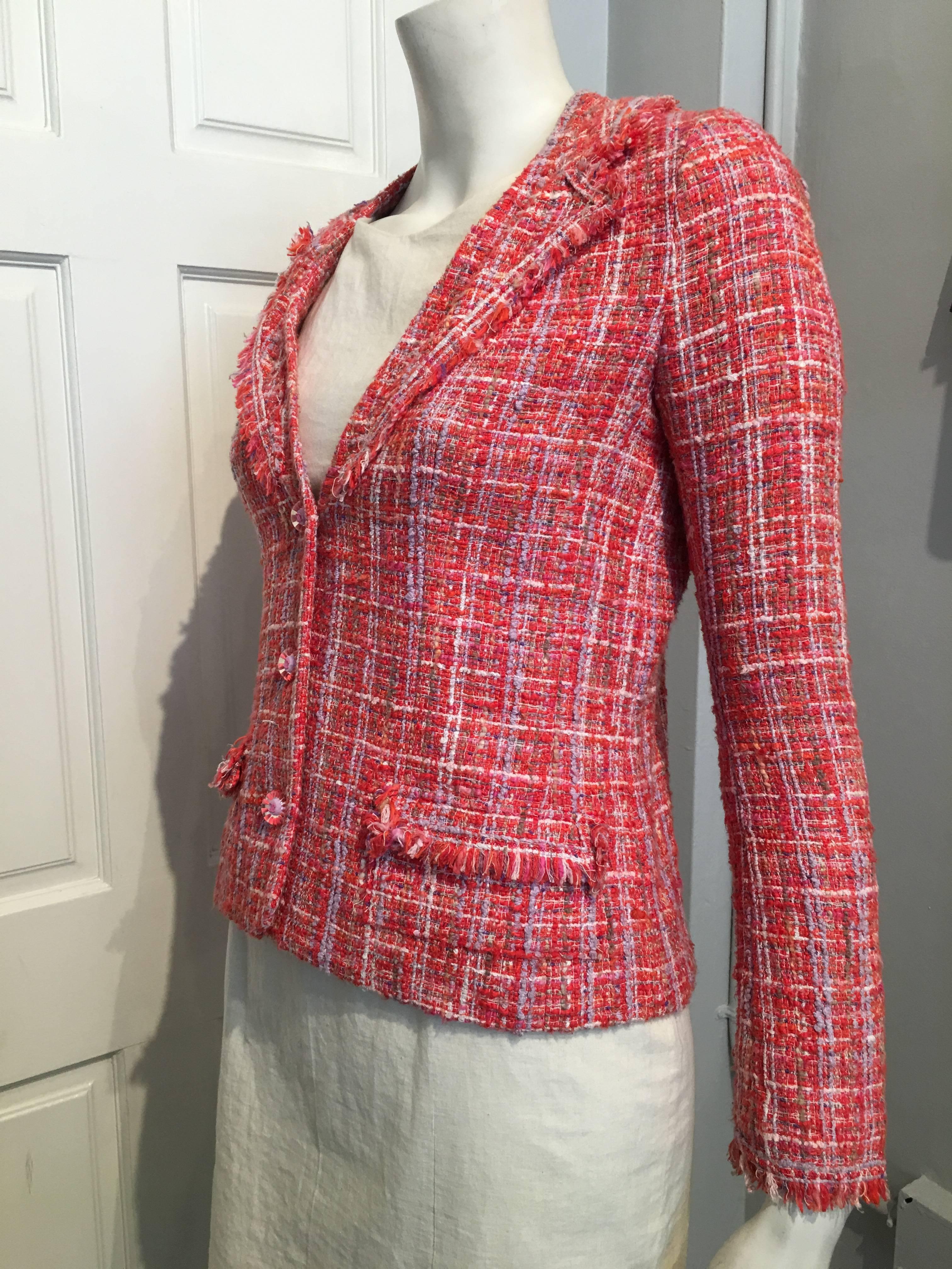 A charming Chanel coral and white tweed jacket with accents of lavender, tan and hot pink. It has fringed faux lapels and fringed shallow pockets, The buttons are clear plastic with the iconic CC logo in pink on white and  surrounded by coral