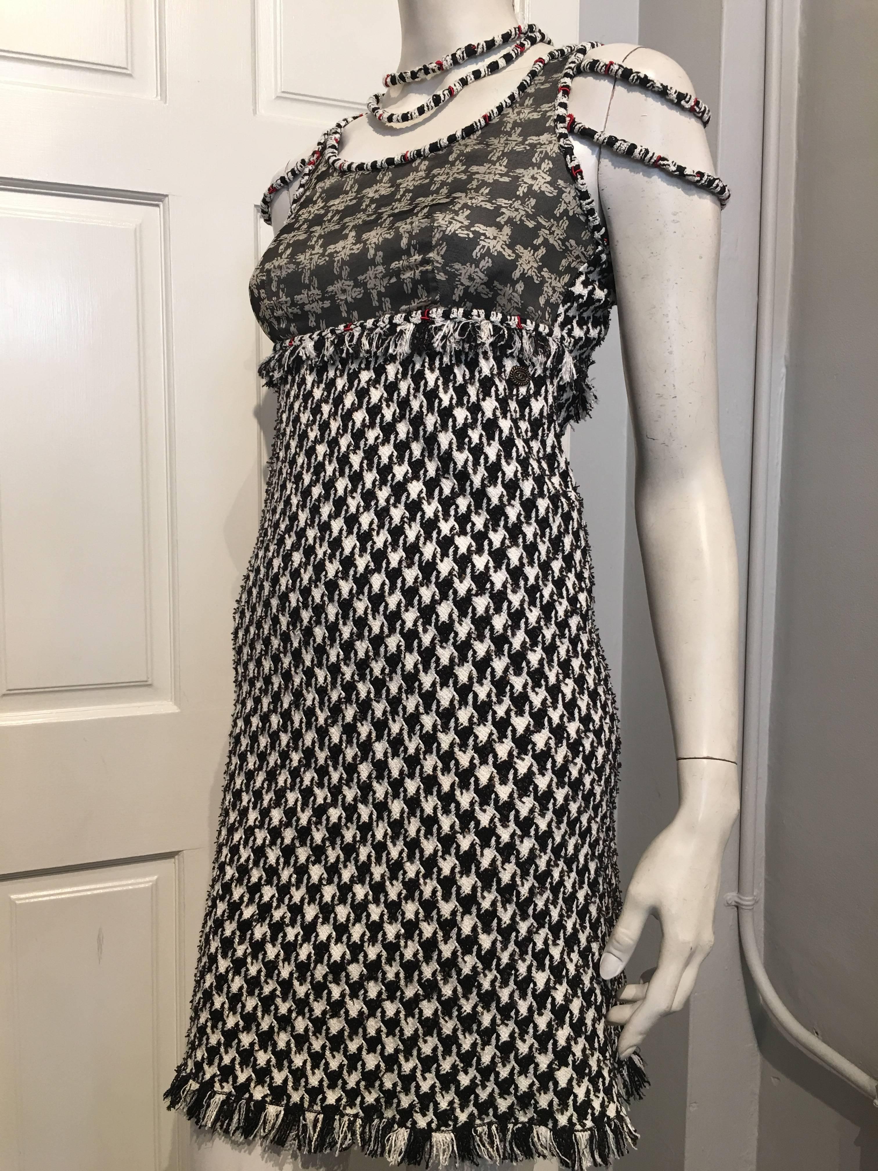 This Chanel dress features a hounds-tooth tweed, with a shear chiffon top printed to match. It is trimmed with woven bands in red, black and white, with matching choker type accent at the neck, and arm cuffs in the same woven fabric that hang just