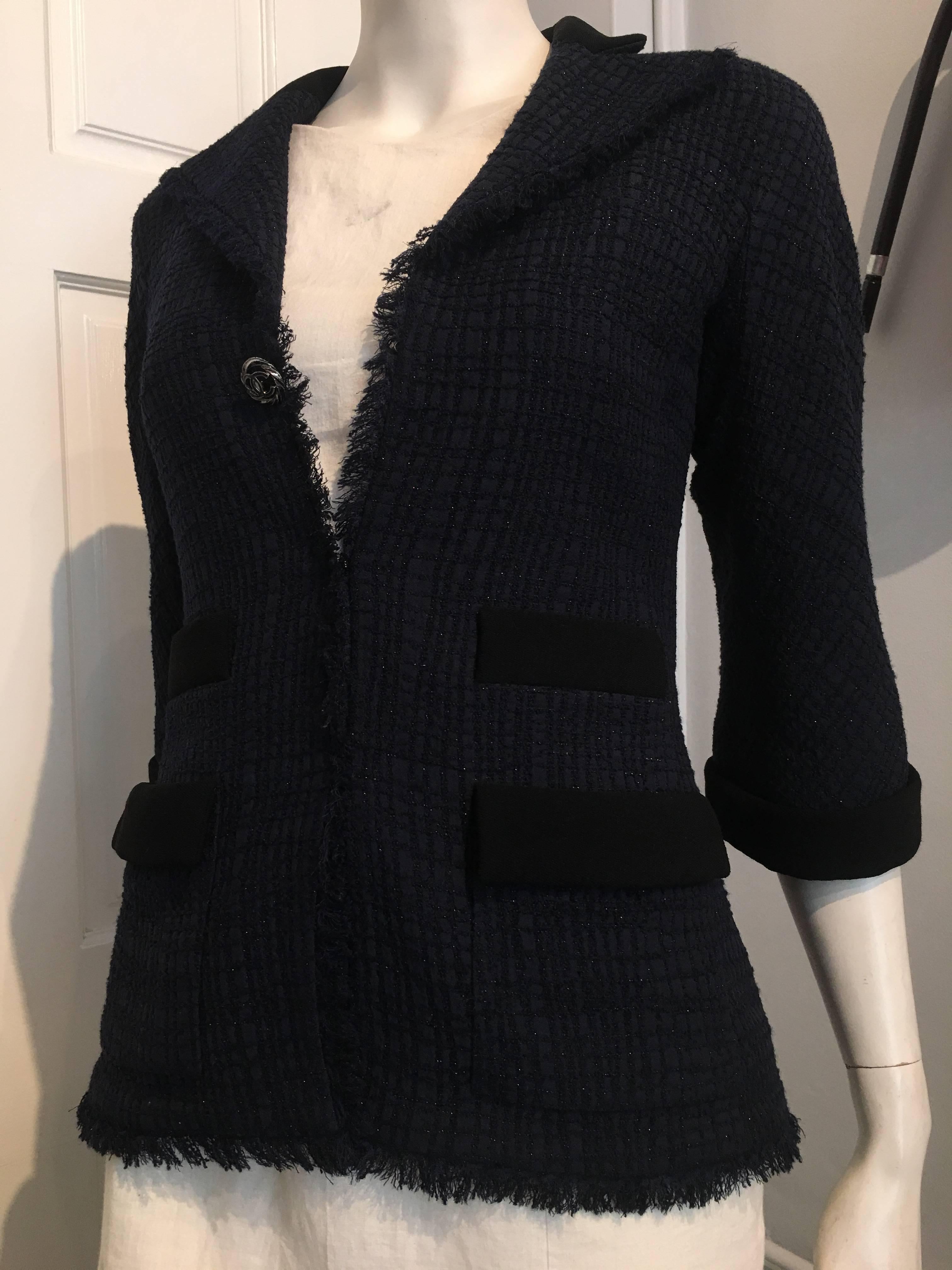 Chanel jacket in a sparkly navy fabric with black accents on collar, cuffs, and pocket flaps, and a narrow,  half inch fringe that runs along the lapels and hem. Each side of the jacket has one real lower pocket and faux top pocket, with black trim