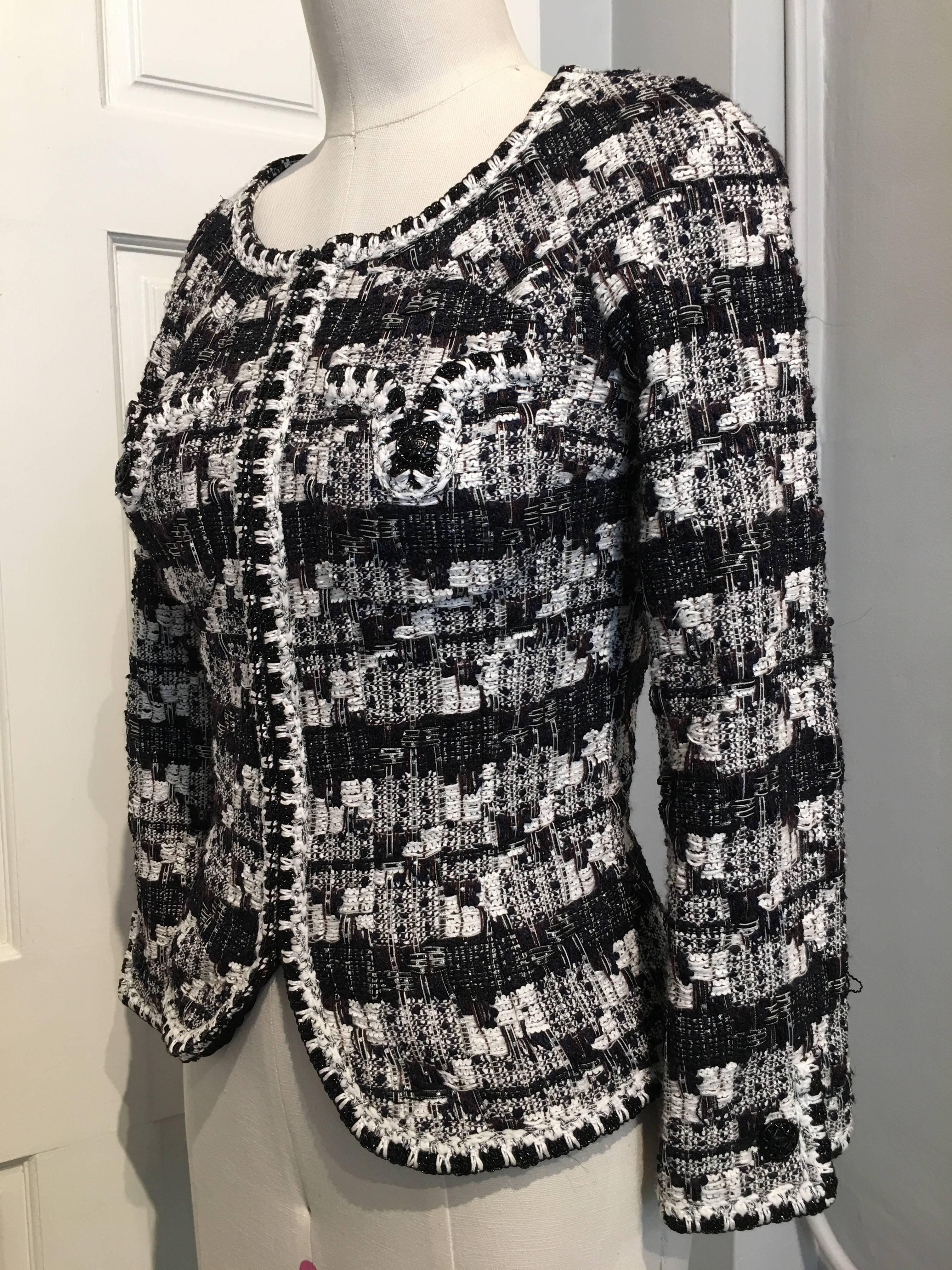 This Chanel jacket from the 2006 Cruise line is in a loose weave in white, navy, brown, silver and black threads. On each of the pockets and cuffs there is a black enameled button in a basket weave design. Small black glass beads alternate white