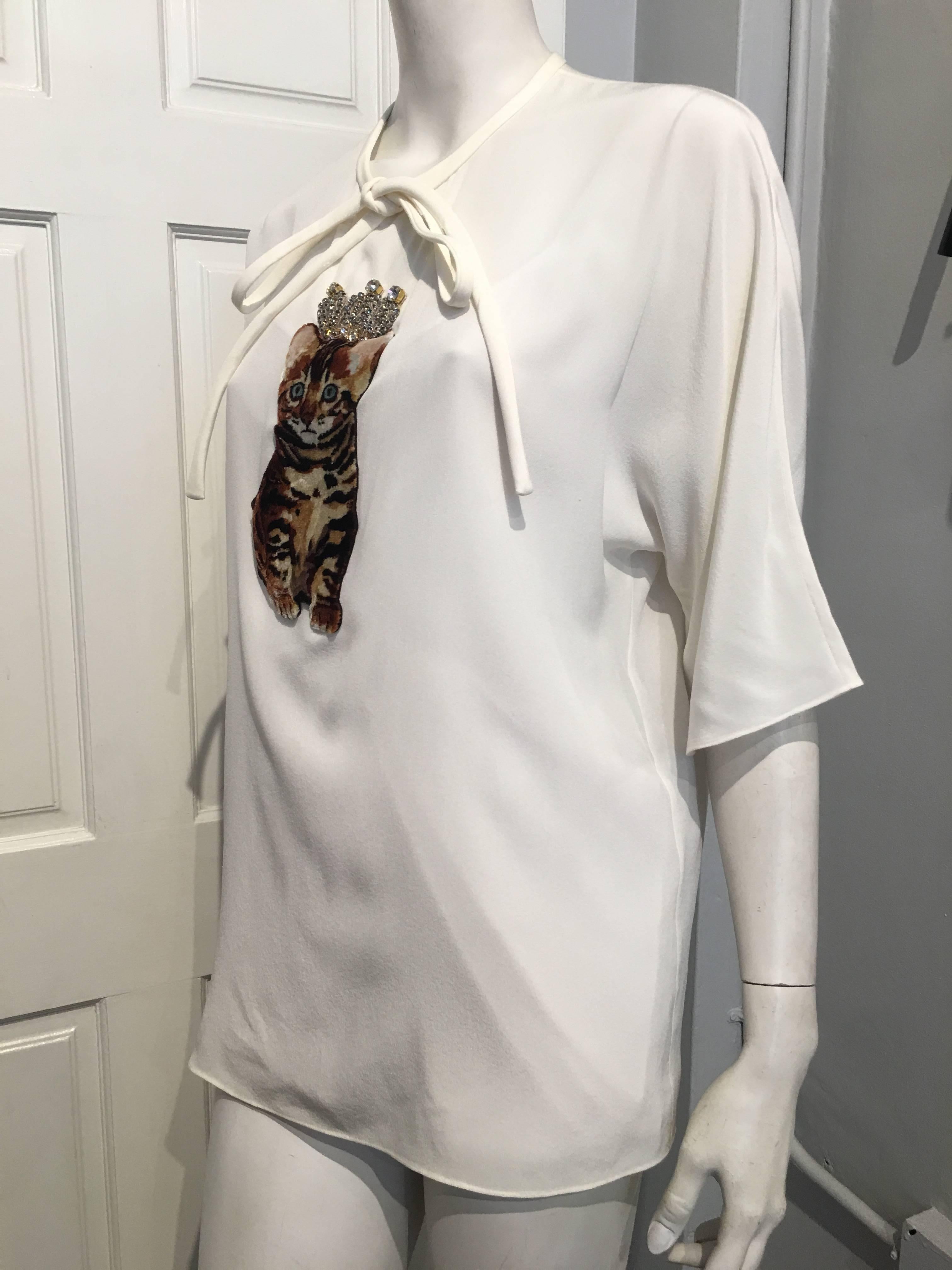 Cream short sleeve top with a rhinestone crowned brown tabby velvet kitten on front. Long ties that can be left hanging or tied in a bow are the front of the neckline for looks. It closes with a single snap button at the back of the neck.