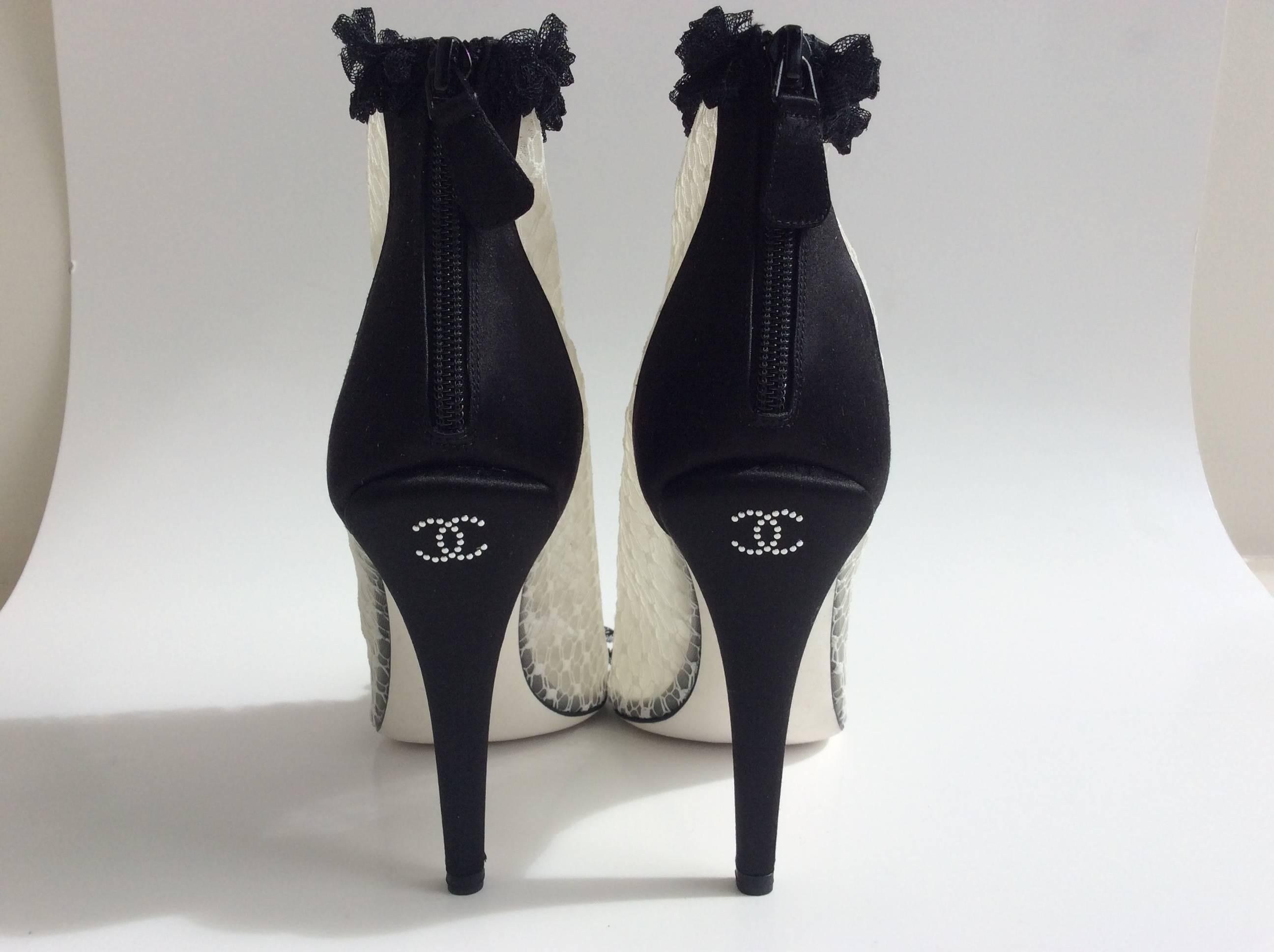  White Chanel lace booties with a black lace trim around the ankles and down the middle of the foot and across the toes. The back of the shoe and the 4.5 in heel are in black satin. The upper part of the heel displays the iconic CC emblem in tiny