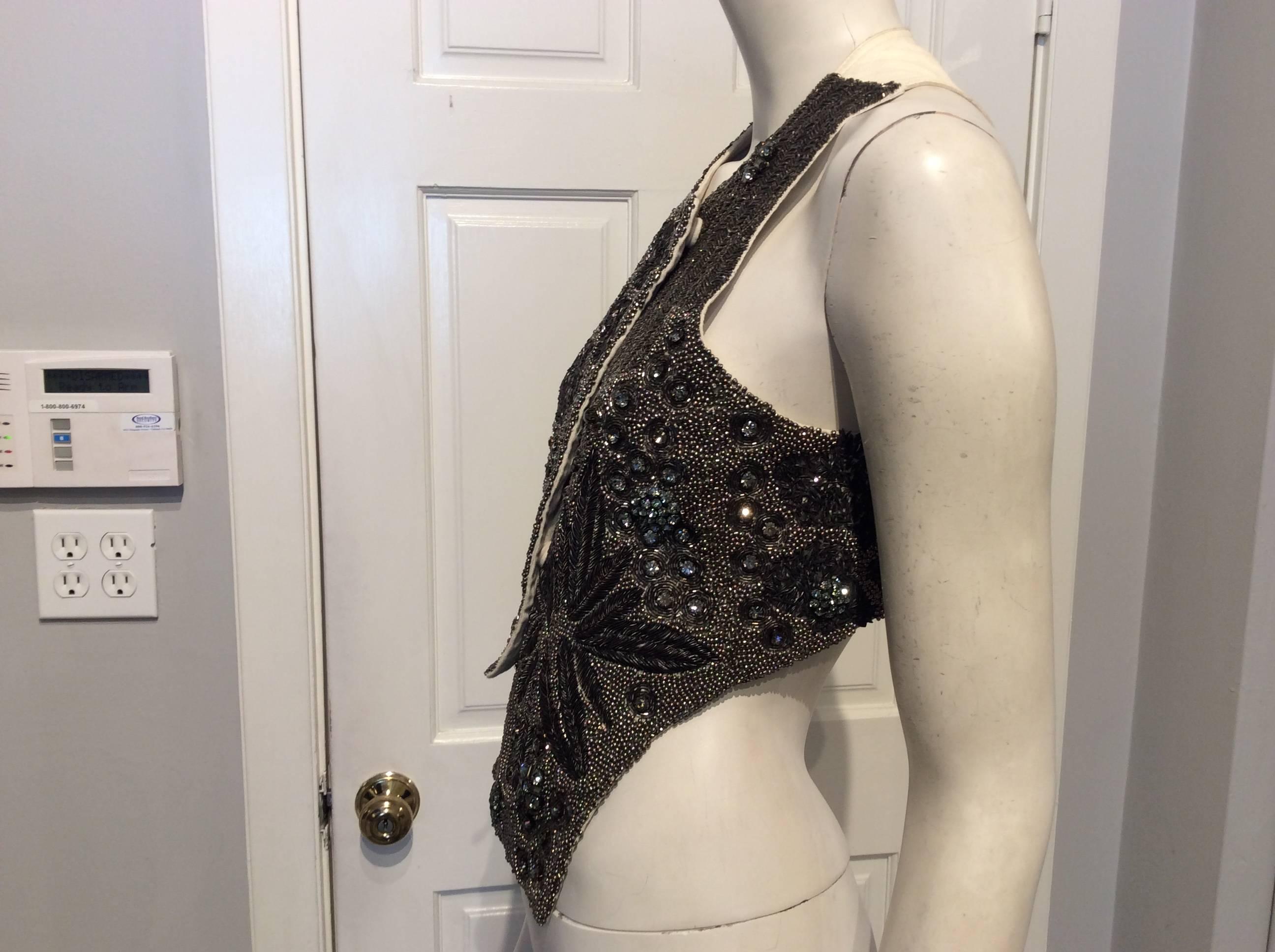 Peachoo + Krejberg pewter beaded vest with white leather in the back. The front left side has a floral like wire thread design, while the rest of the vest is covered in beads and different size rhinestones. The right side of the vest is 14.5 in