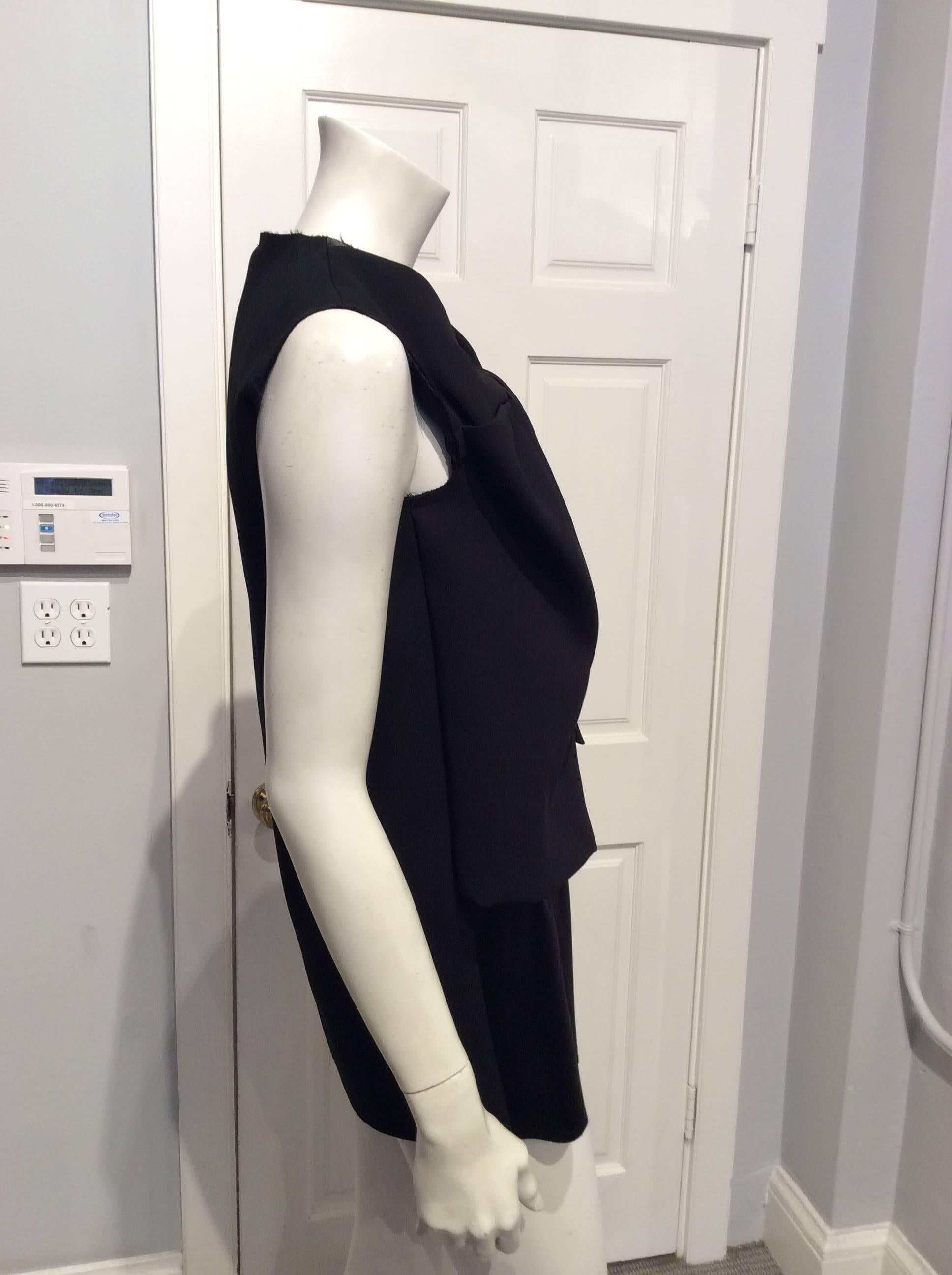 Sleeveless black top with a shiny under-layer that is partially covered with a mock vest of different fabric.  The top layer is of uneven length with a twist detail.  All seams have a raw edge.  