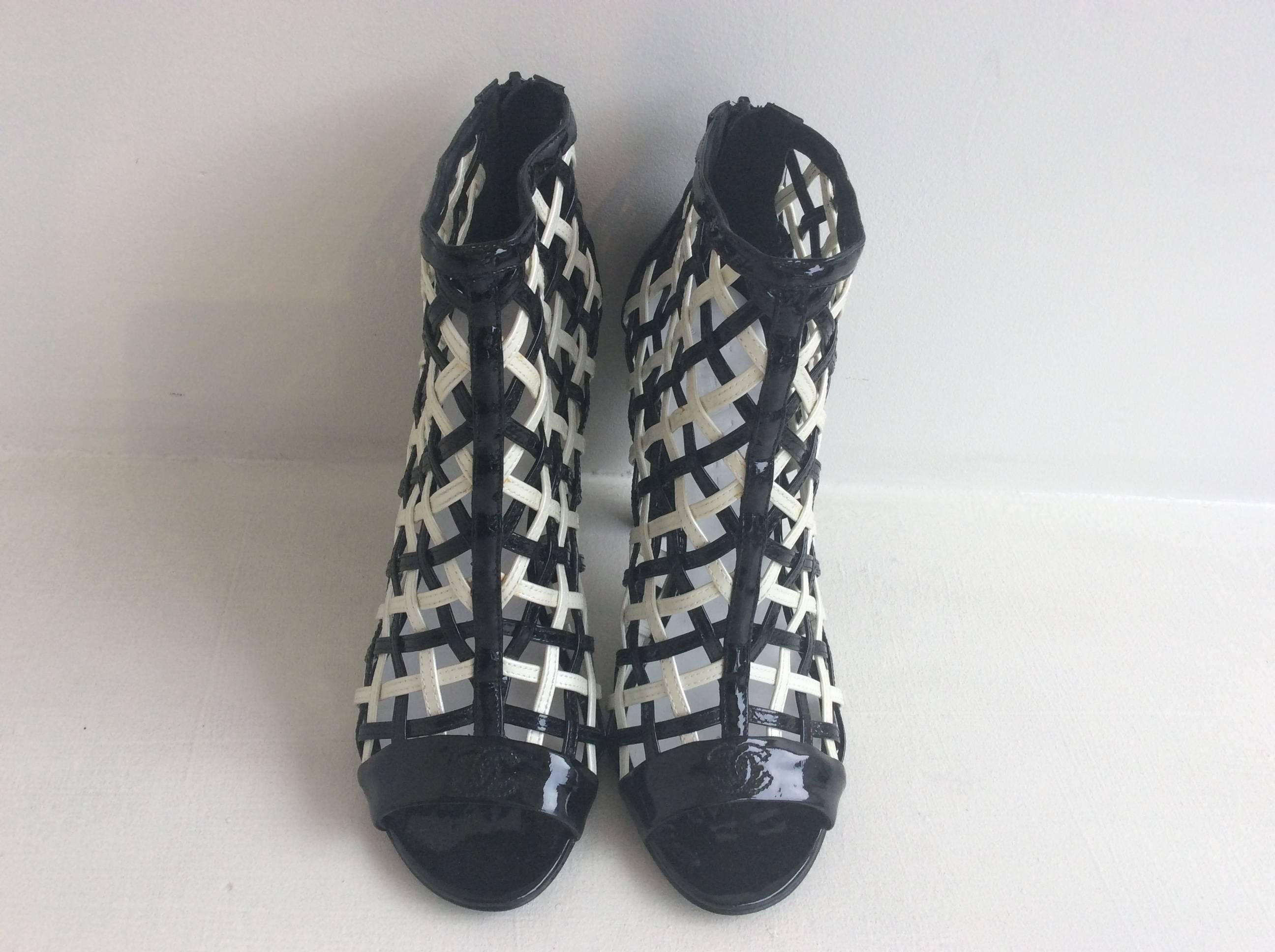 Chanel black and white patent open toe caged booties with the iconic stitched double CC on the toe band. They have a sculptural black plastic spiral 4 1/4in heel. The closure is a 3.5in zipper in the back.