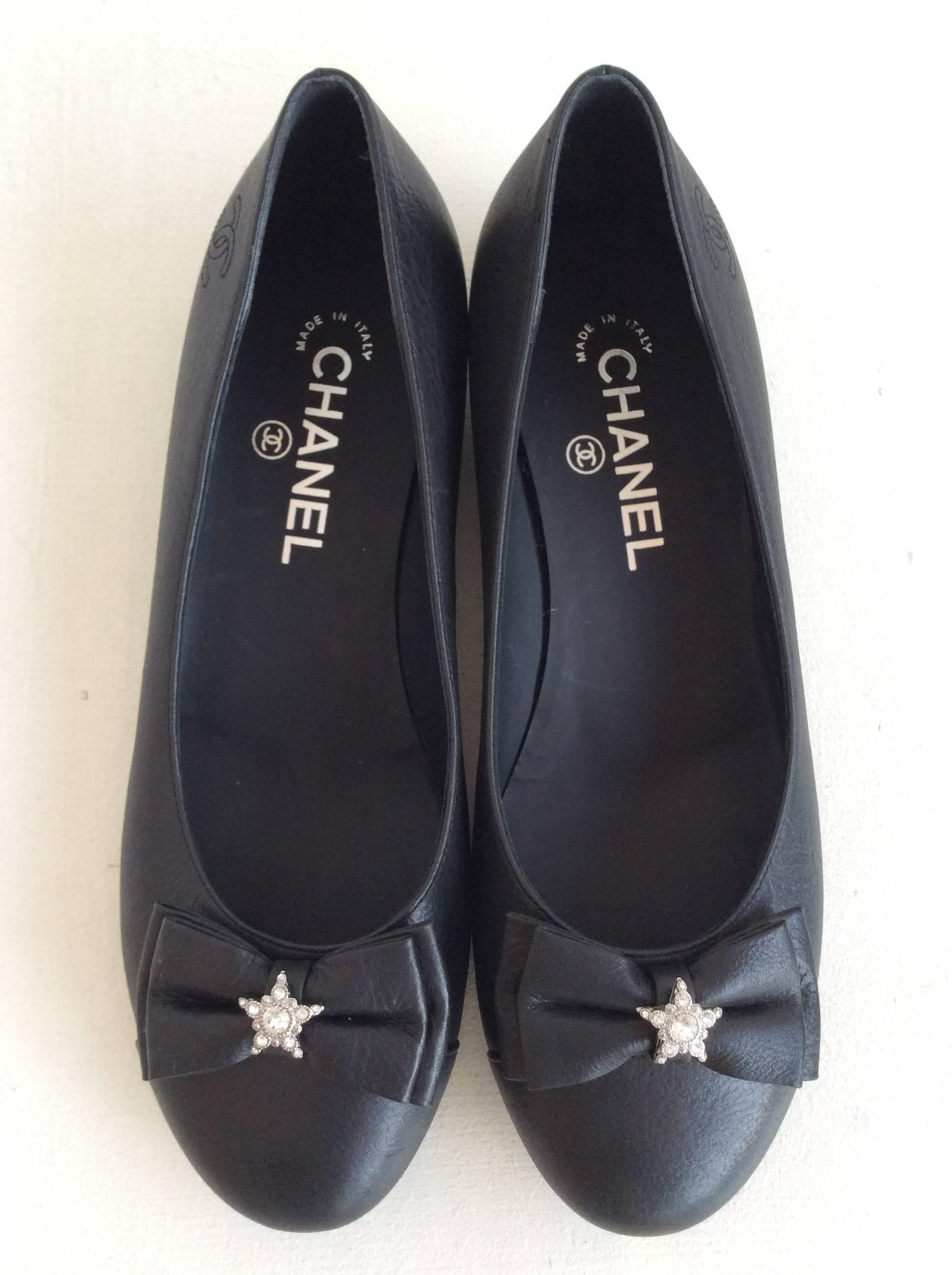 Chanel black leather ballerina flats with bow detail on the toe. The center of the bow has a small clear rhinestone star as an accent.