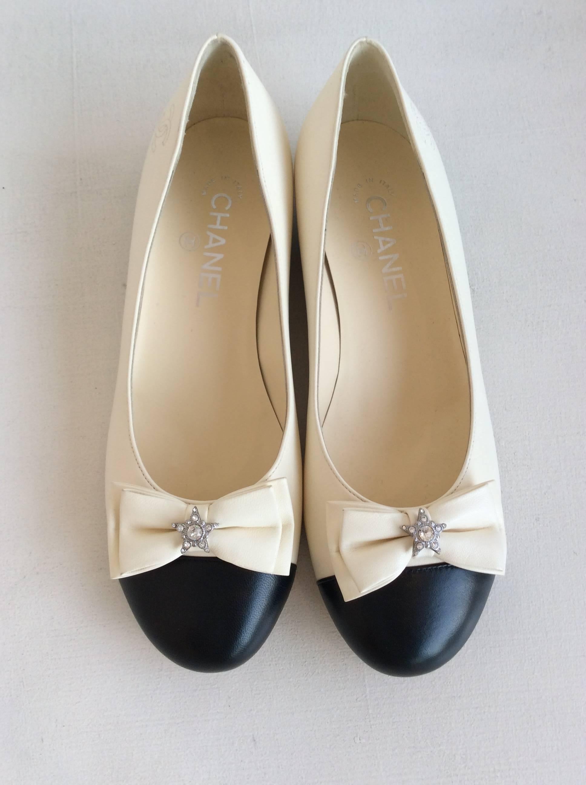 Chanel white leather ballerina flats with black toe. The front is embellished with a white leather bow that has a small clear rhinestone star in the middle.