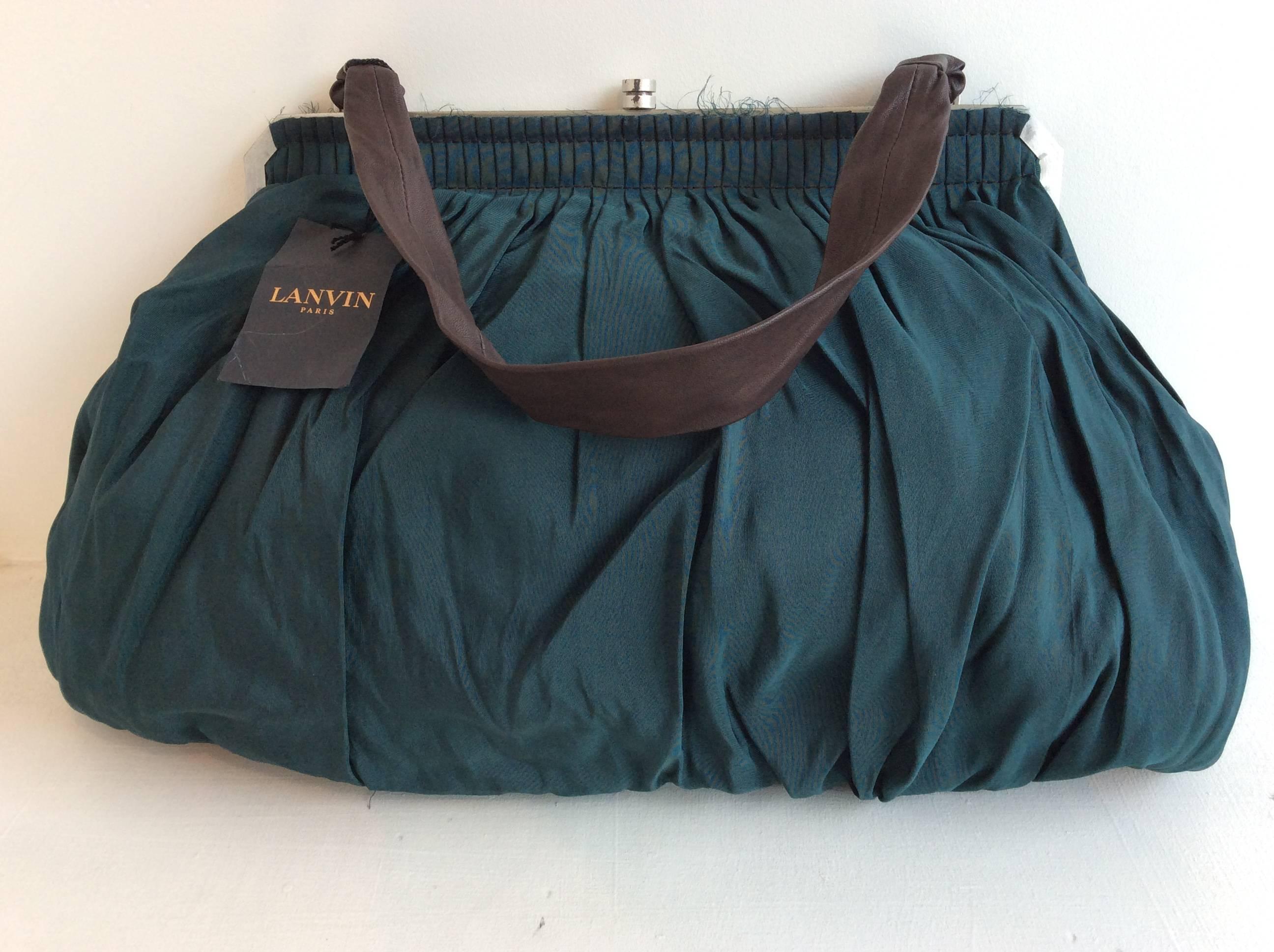 Amazing retro looking bag in forest green silk failed with unfinished seams. It has a brown single 1 1/2in wide and 21 1/2in long strap. The metal frame is muted silver. The lining is black fabric. 

Please note that the clasp has some black