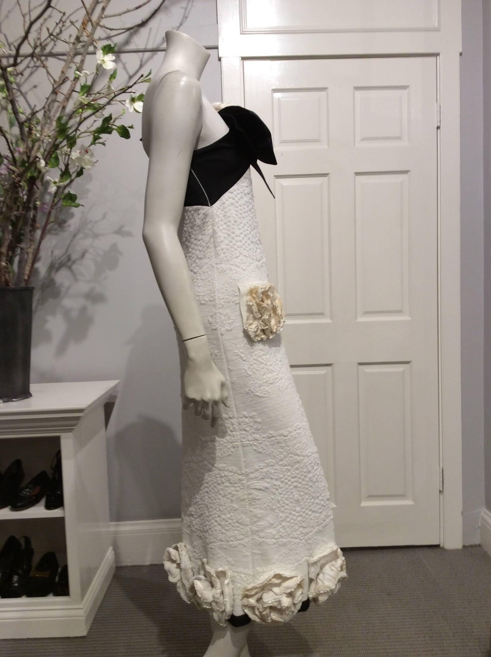 Chanel one shoulder black and white knit gown. The big black bow on the shoulder has a large ivory sequin flower in the middle of it. There are two pockets on the front on the hips hidden with two large sequin flowers. The bottom of the gown is a