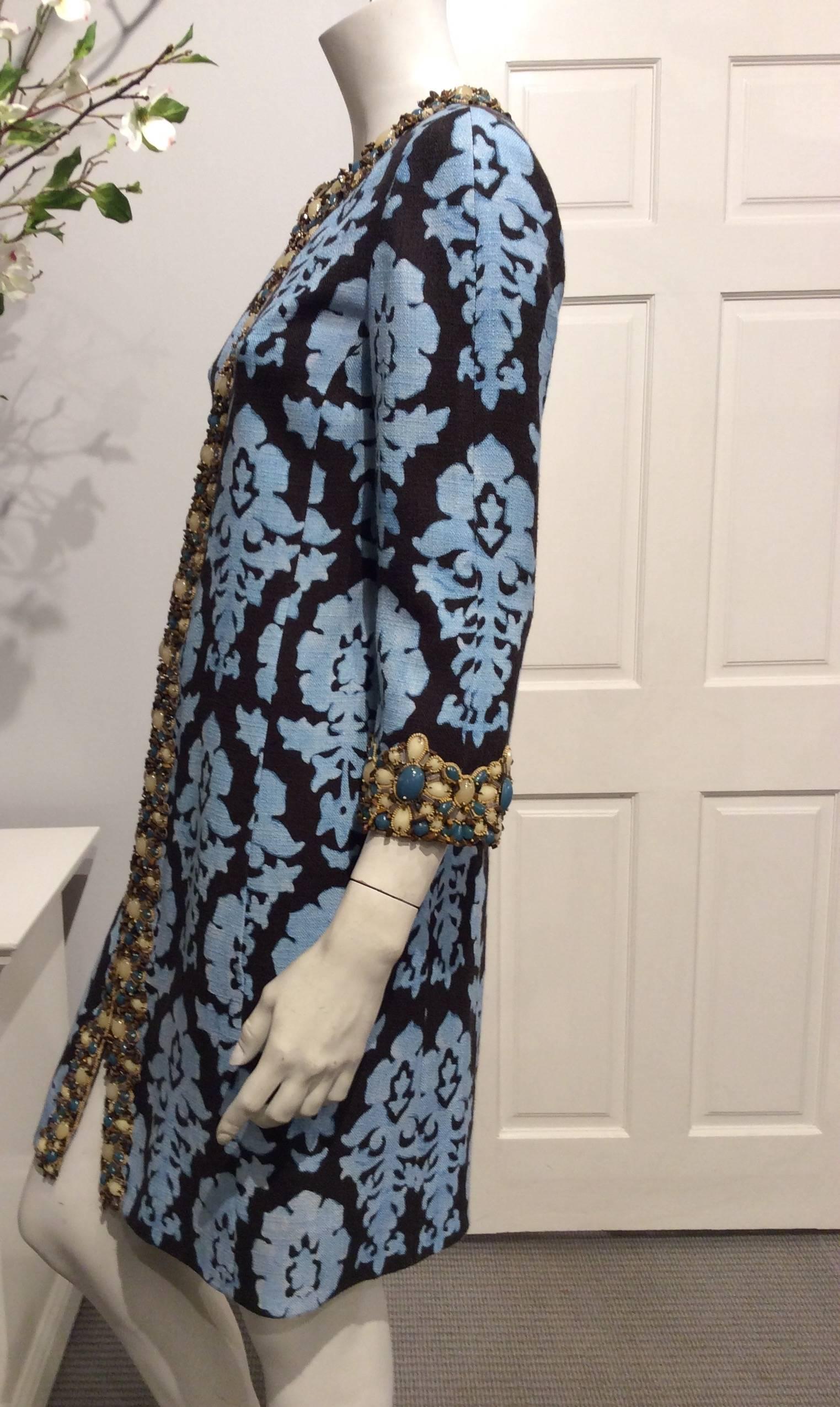 Andrew GN coat in light blue oversized paisley print on a dark brown background. The beaded trim is made out of different kind of stones in shades of brown, taupe and teal blue. It closes with 10 pewter colored hooks. The sleeves are 3/4 length.