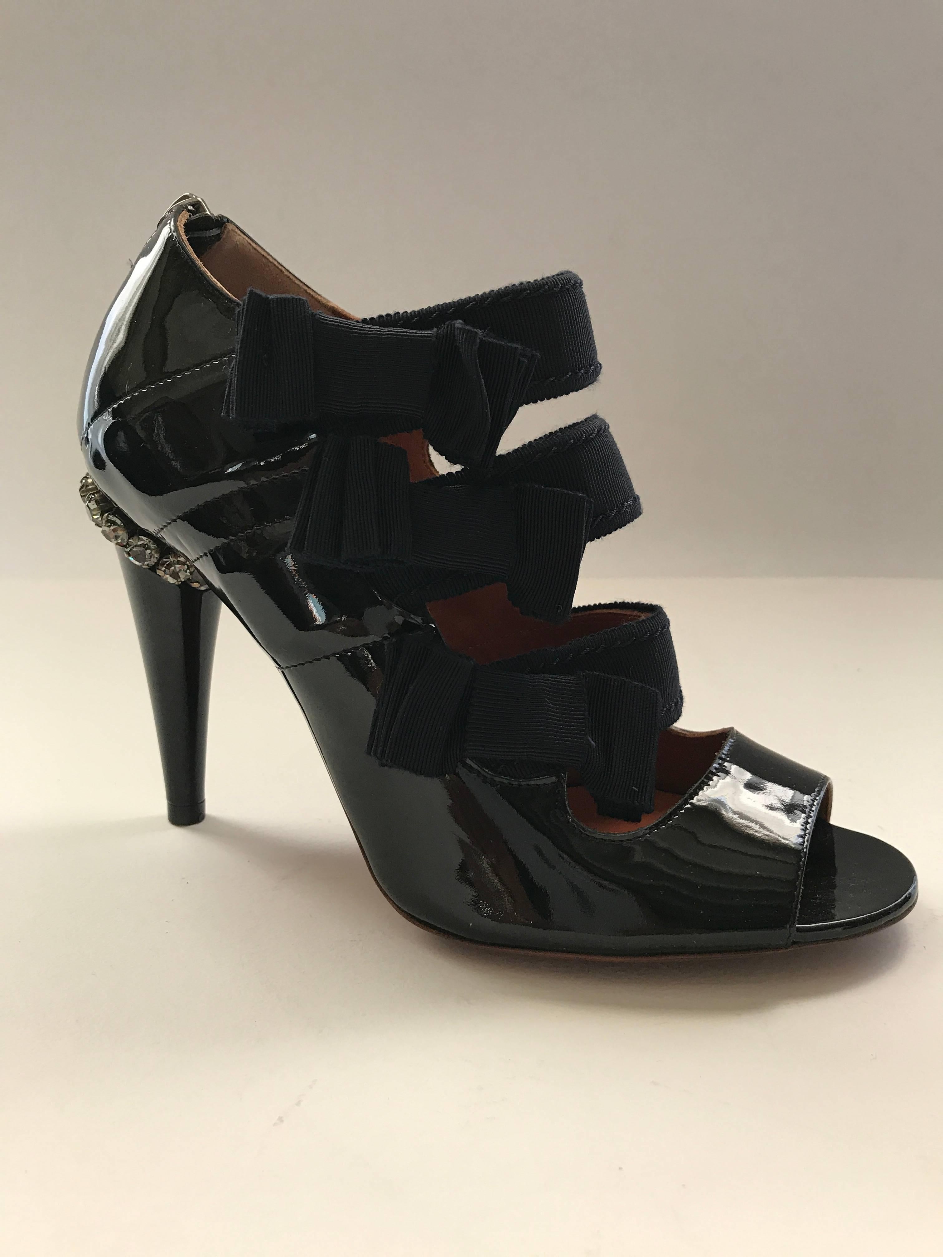 Amazing Lanvin sandal booties in black patent leather from the 2009 summer collection. The three inch wide grosgrain straps are embellish by flat bows on the sides. The 4 inches cone heel is encircled at the top by a row of pewter crystals. The shoe