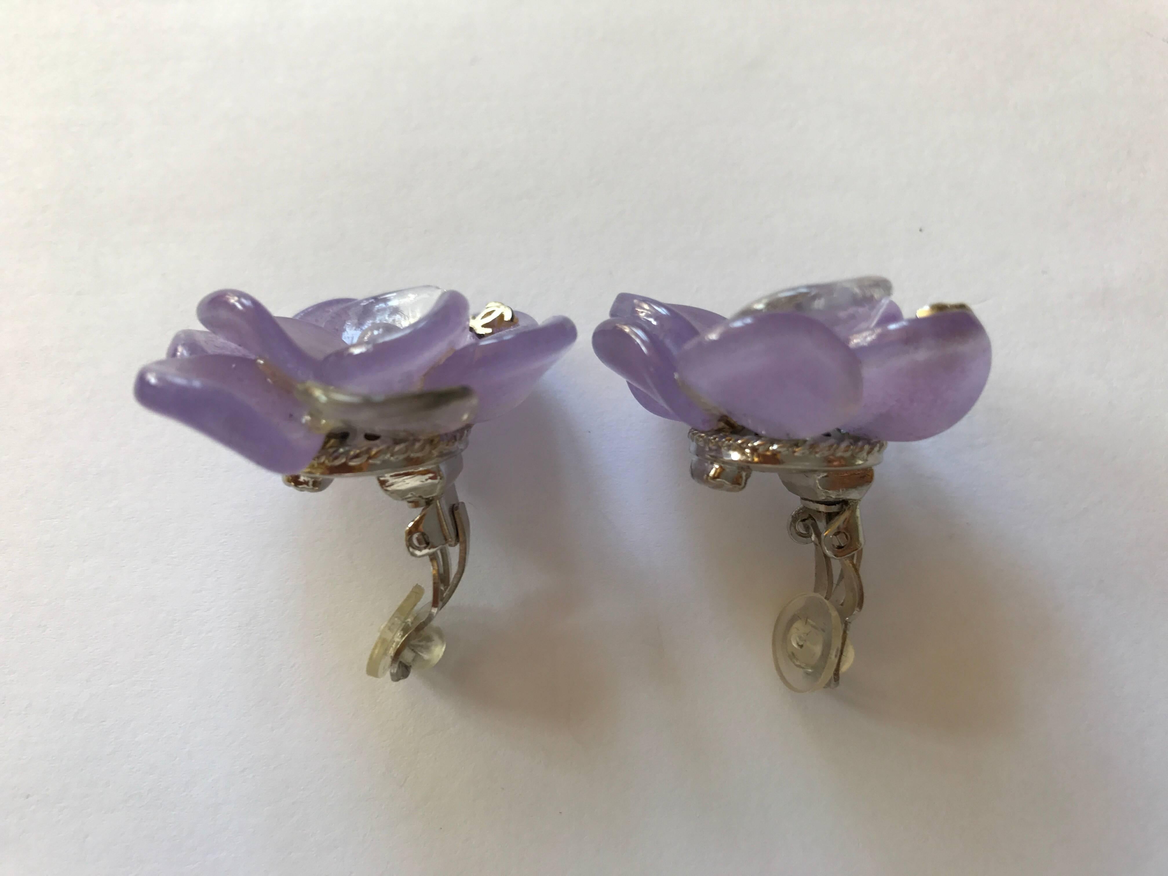 Chanel purple Gripoix camellia clip on earrings from the 2001 Spring collection with two small iconic silver CC.
The flower is composed of seven lavender petals and two clear ones. They are approximately 1.25 inches in diameter. They are brand new