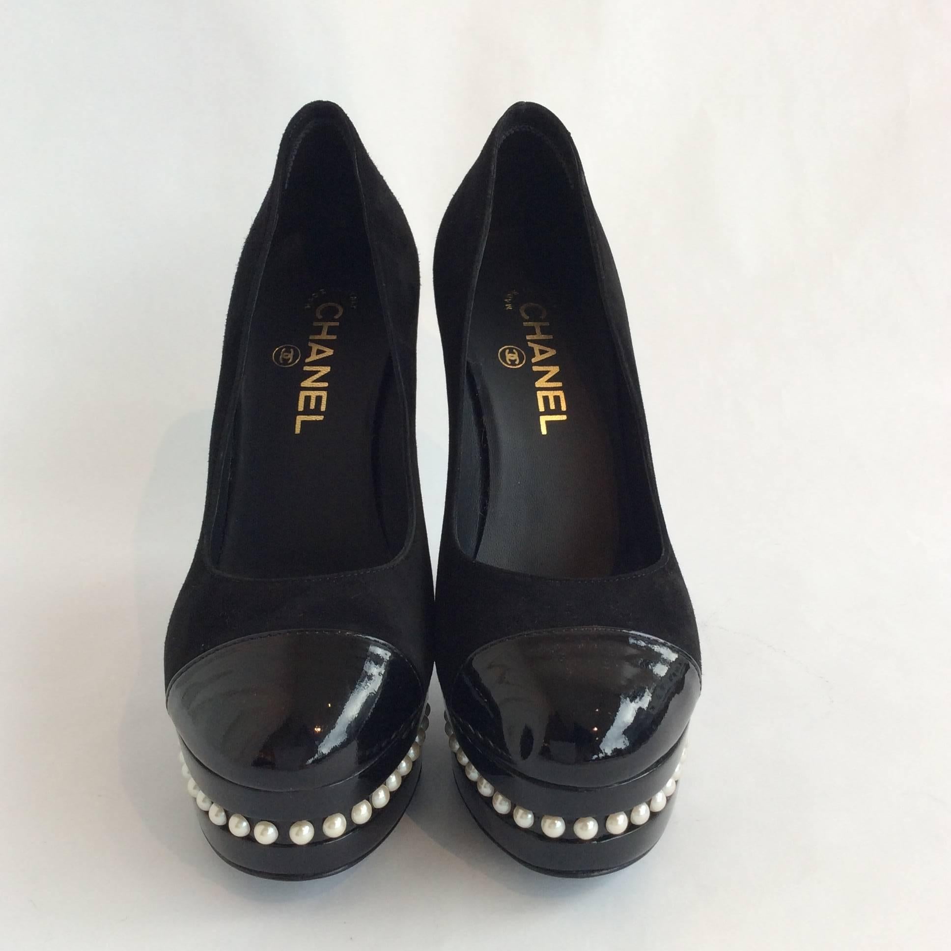 Chanel platform pumps in black suede with black patent tips. The black acrylic platform is 1.25in high and has a single row of pearls going through the middle. The acrylic heel is 5in high and has two rows of pearls in the upper half.