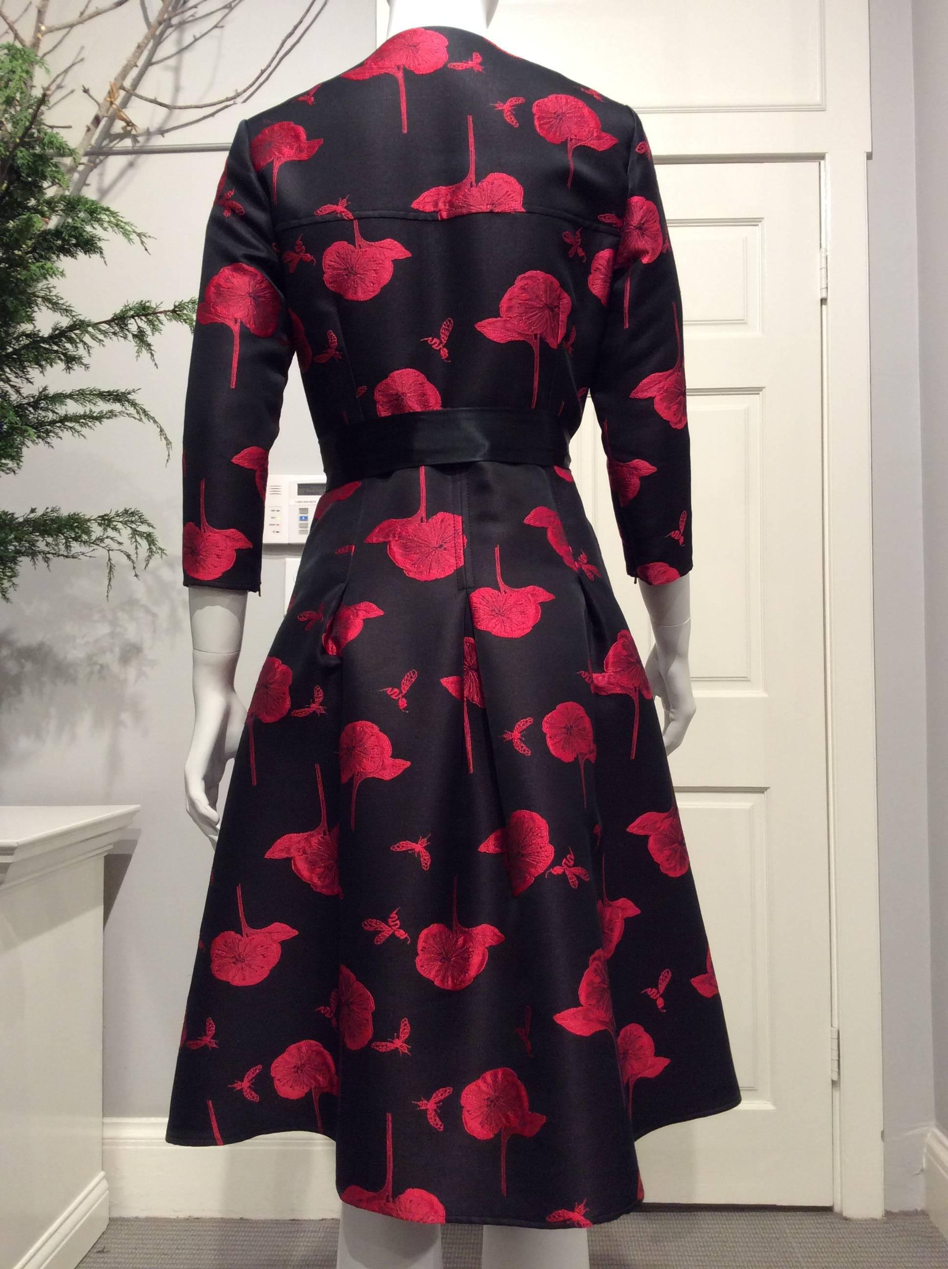 Coat dress in a black and magenta floral pattern. The narrow sleeves are 3/4 length and close with a hidden 4in long zipper on the inside seam. It closes in the front with eleven small black buttons. The top is lined in black silk. The soft pleats