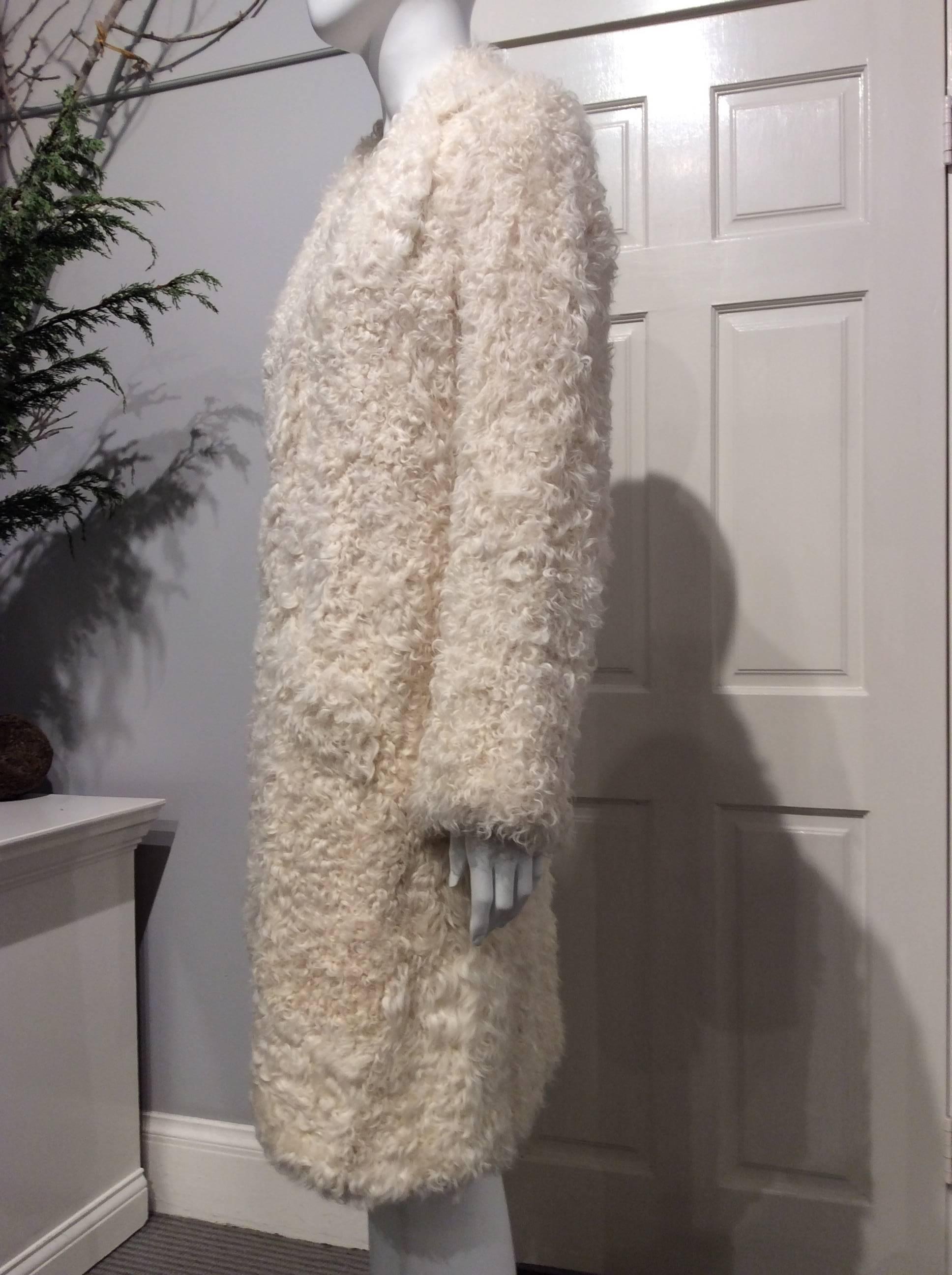 Single breasted coat in ivory curly lamb with twisted collar. It closes with 3 oversized ivory buttons. The coat has two slanted front pockets.