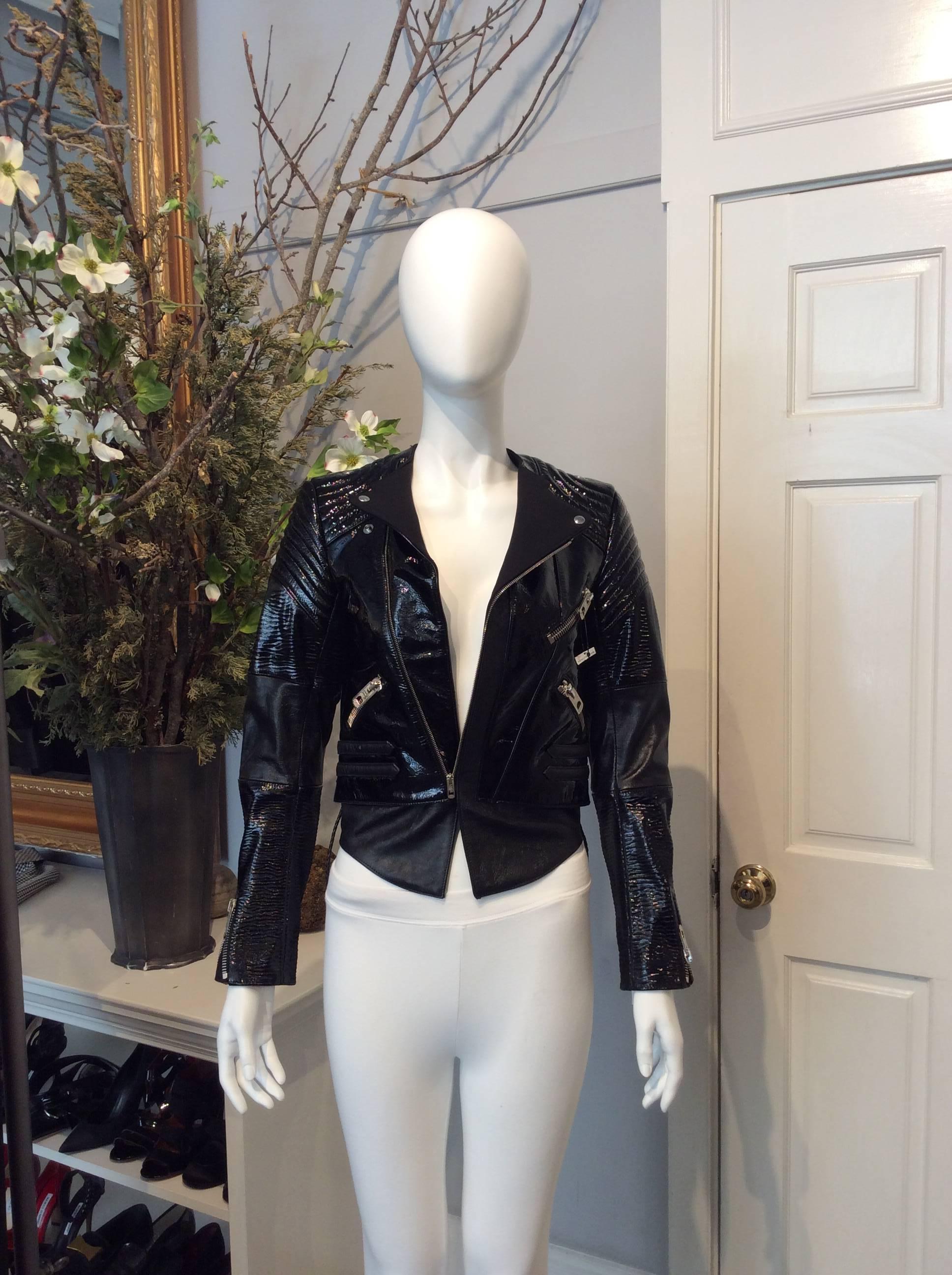 Black Balenciaga textured patent leather motorcycle jacket. Soft black lambskin on elbows and base of jacket. Assymetrical zippers on front and snap closures at lapels. Dual pockets. Dual draw strings at back. Zippers at sleeve cuffs. Cut for a very