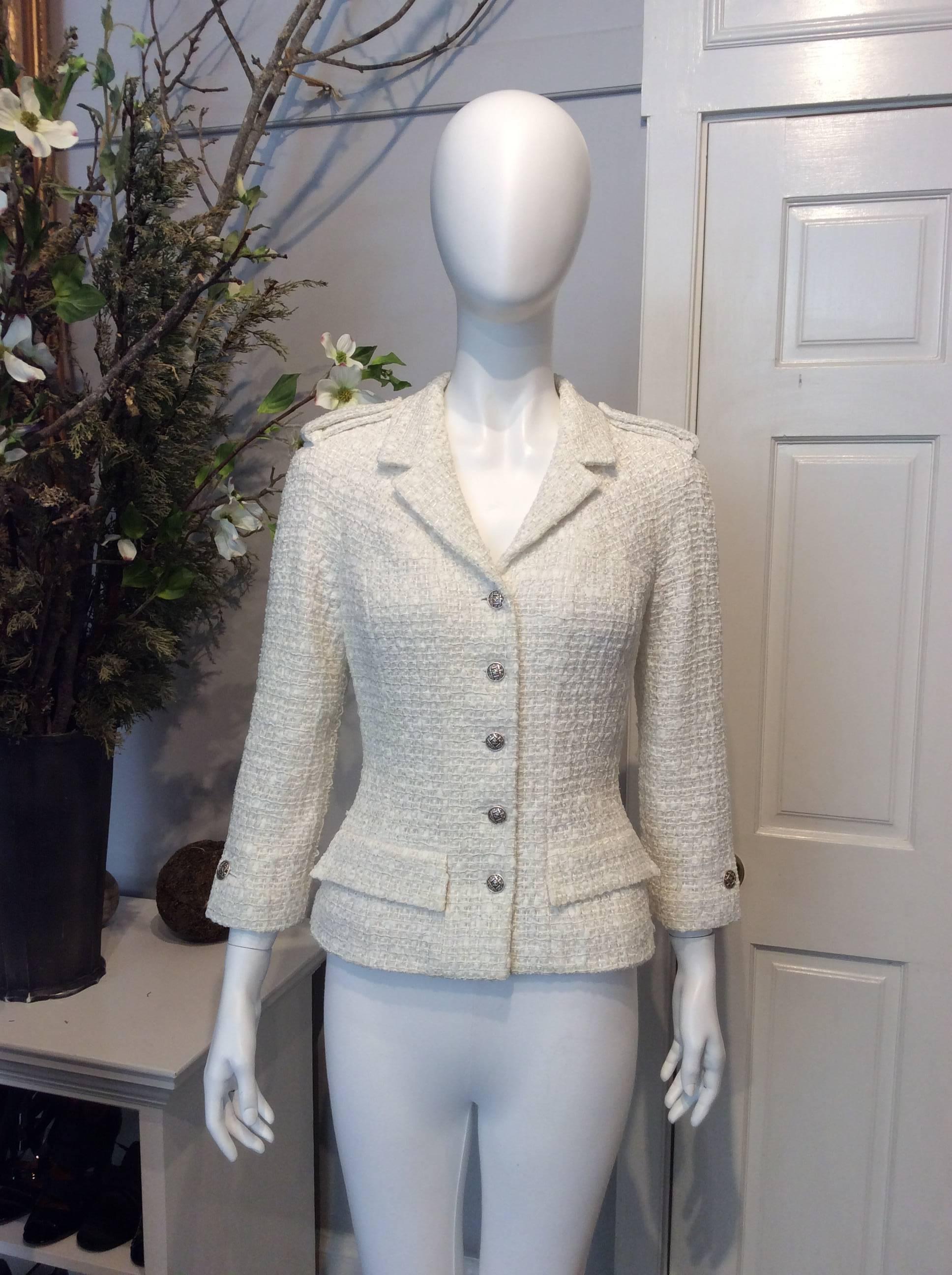 Classic cream Chanel tweed jacket with silver threading accents throughout. Six silver buttons at front with Chanel detailing. Buttoned epaulets at each shoulder Single button at each cuff. Silk lining with signature Camellia print. 

Sizing: Fr38,