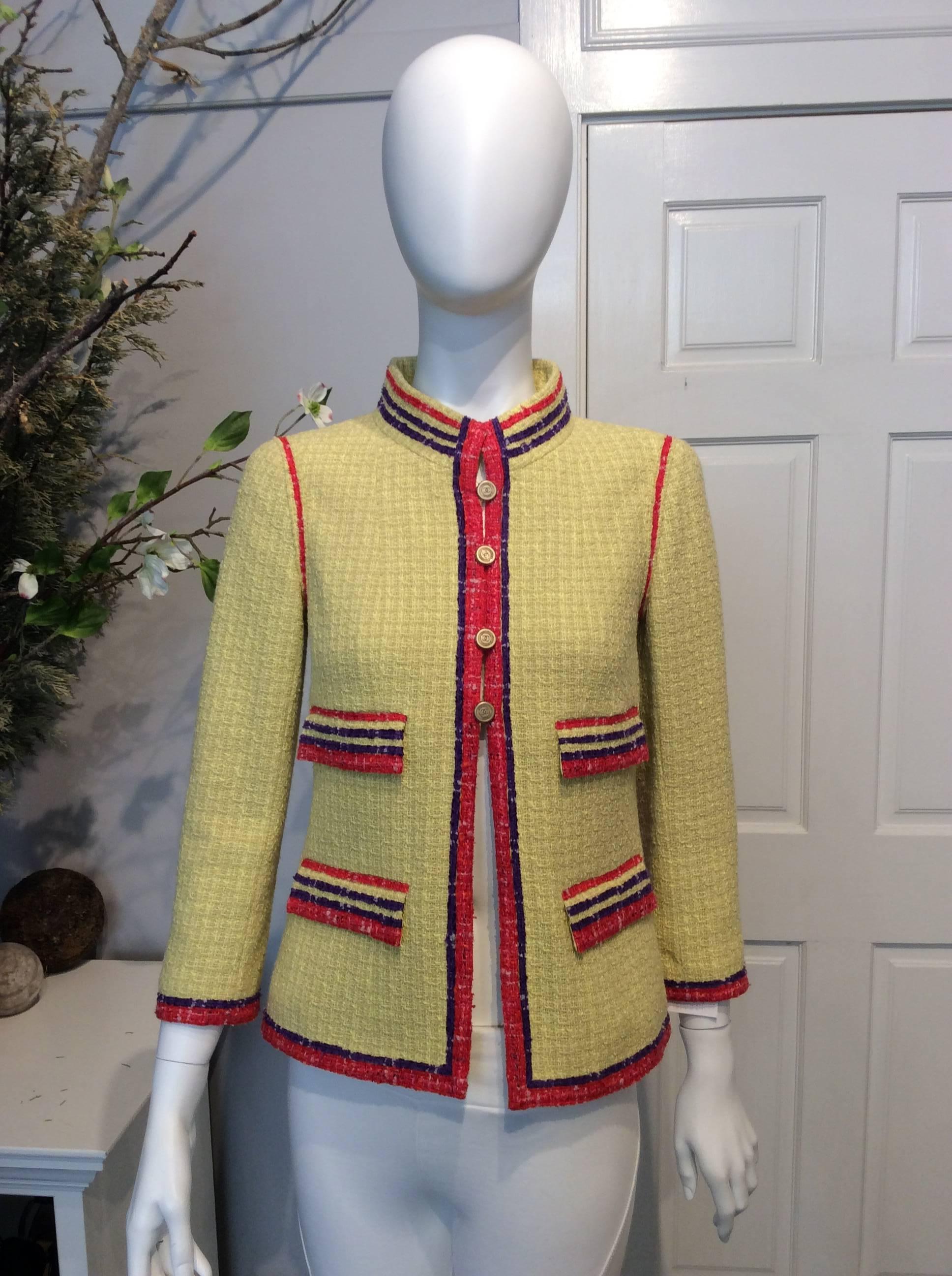 Chanel yellow tweed high-collared jacket with purple and red stitched trim throughout. Four pockets with yellow, red, and purple detailing. Five gold bottlecap “CC” button closures at front, two buttons at each sleeve, and three buttons at side