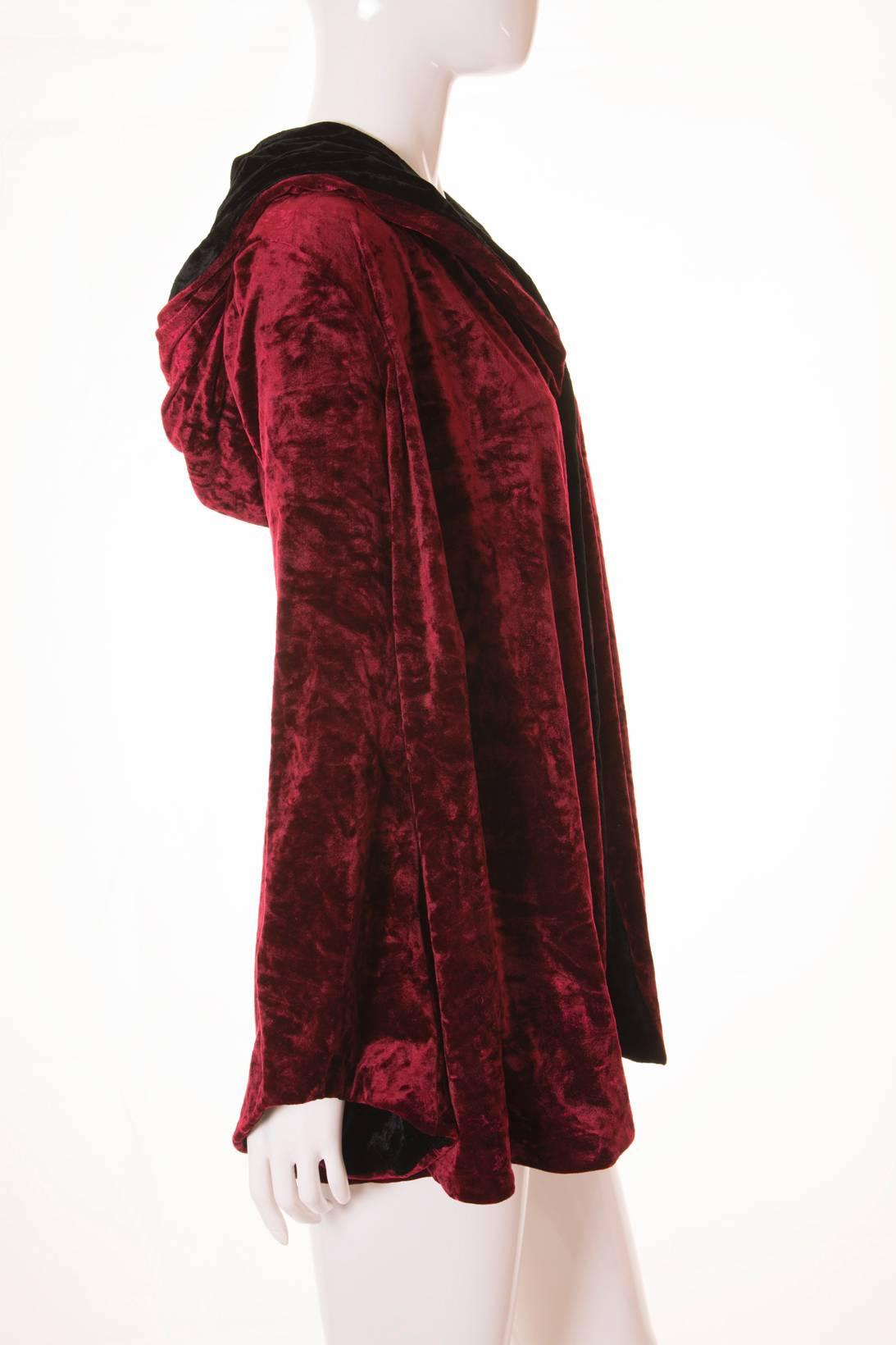 This hooded velvet cape jacket by Norma Kamali is made of sumptuous maroon and black velvet. The contrasting black crushed velvet lining is visible on hood and also on the collars. Deep hood. Exaggerated trumpet sleeves. Stretch in fabric. The front